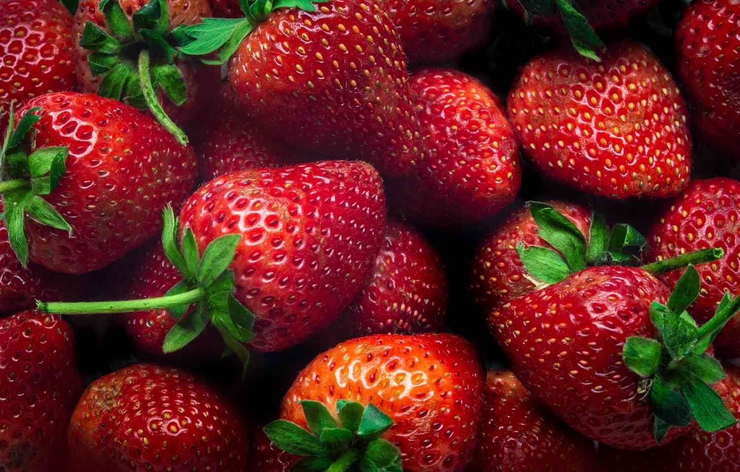 Close-up of fresh red strawberries with green leaves filling the frame