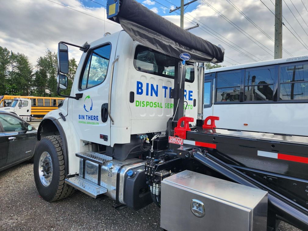 White tow truck with flatbed and toolboxes parked outdoors under a cloudy sky