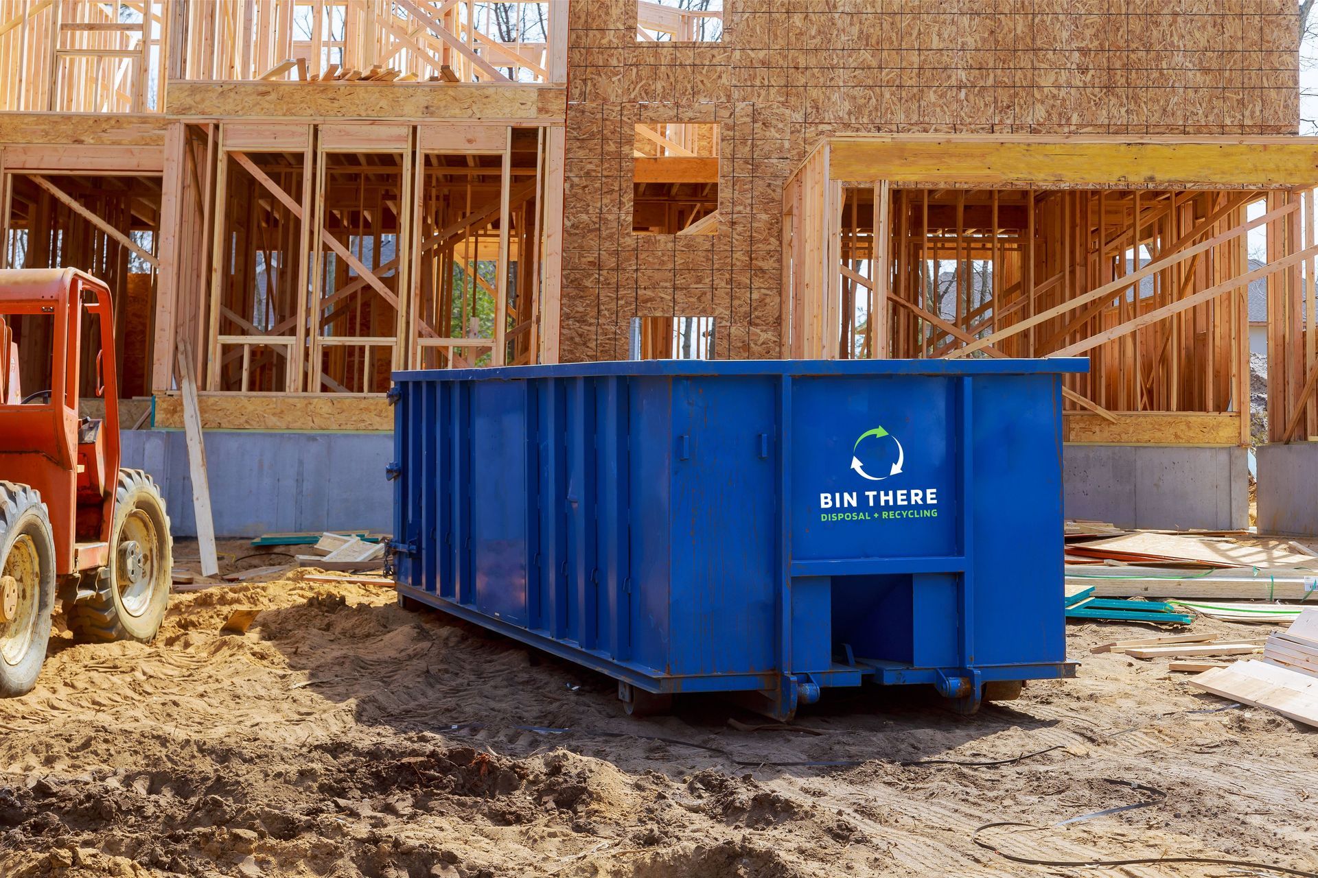 Blue construction dumpster in front of a wood-framed house under construction