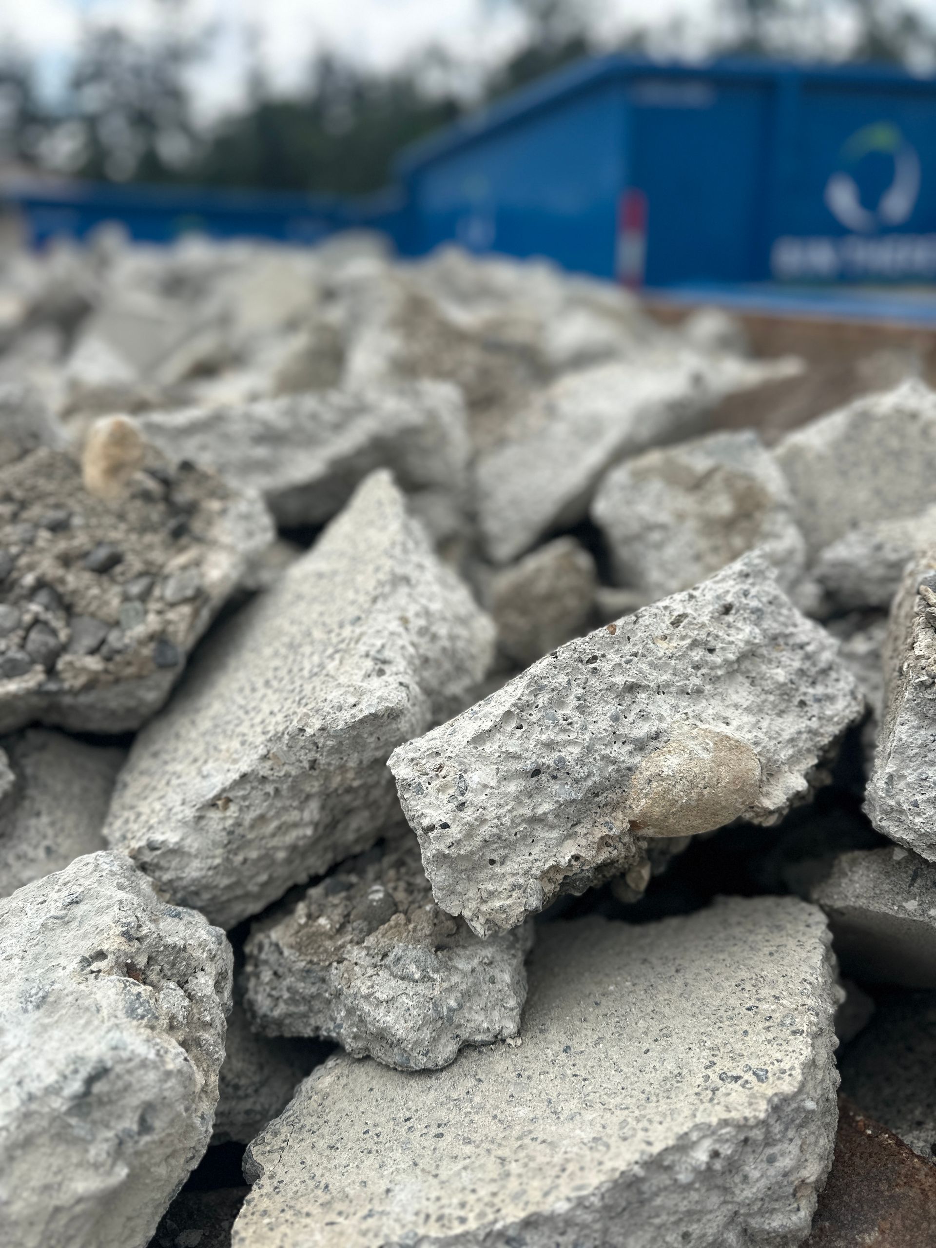 Pile of gray rubble and broken concrete with a blue industrial building blurred in the background