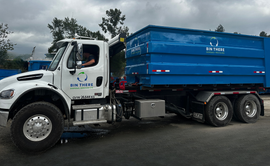 A dumpster is parked in a driveway in front of a house.