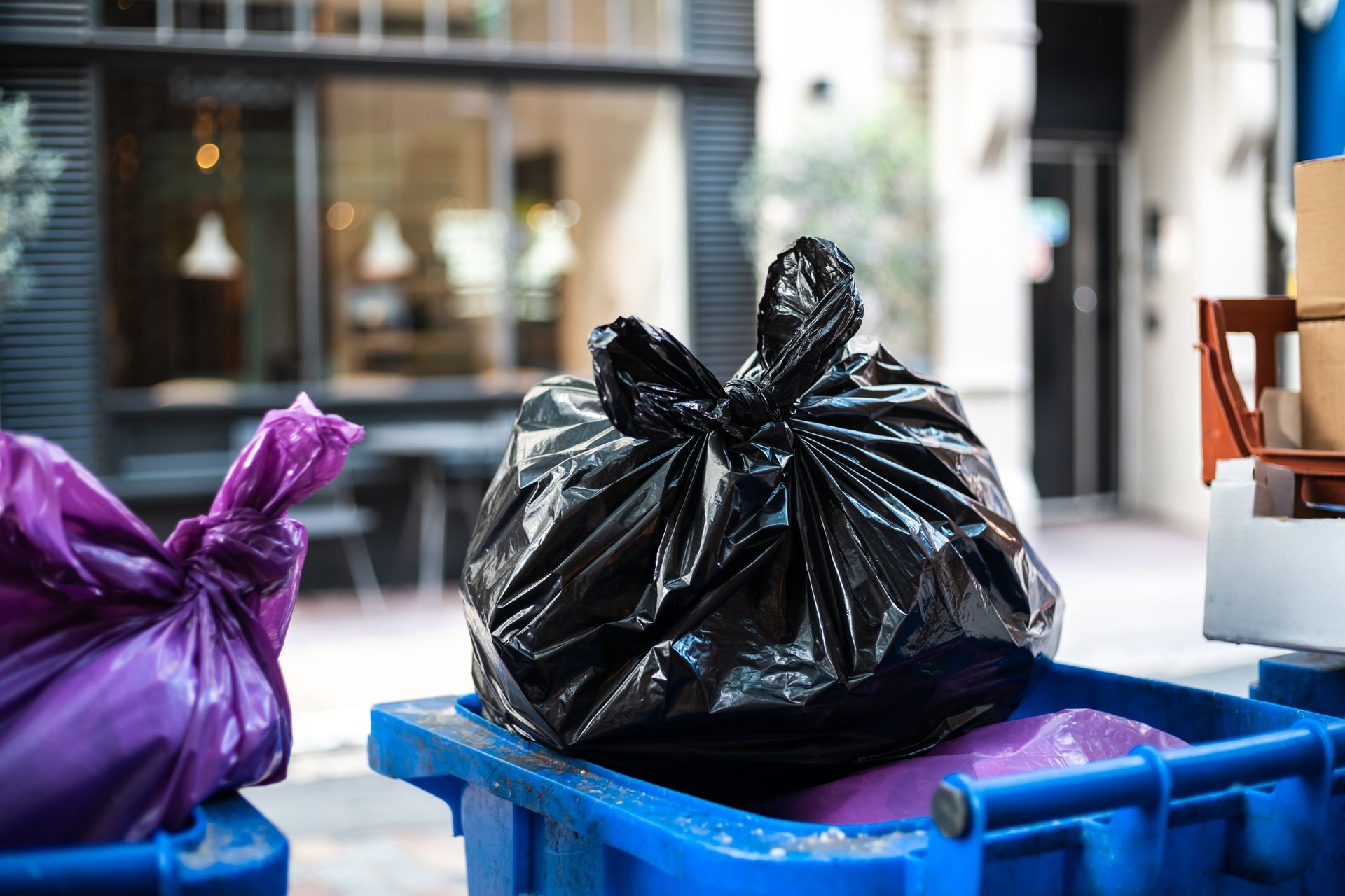 A blue trash can filled with purple and black trash bags.