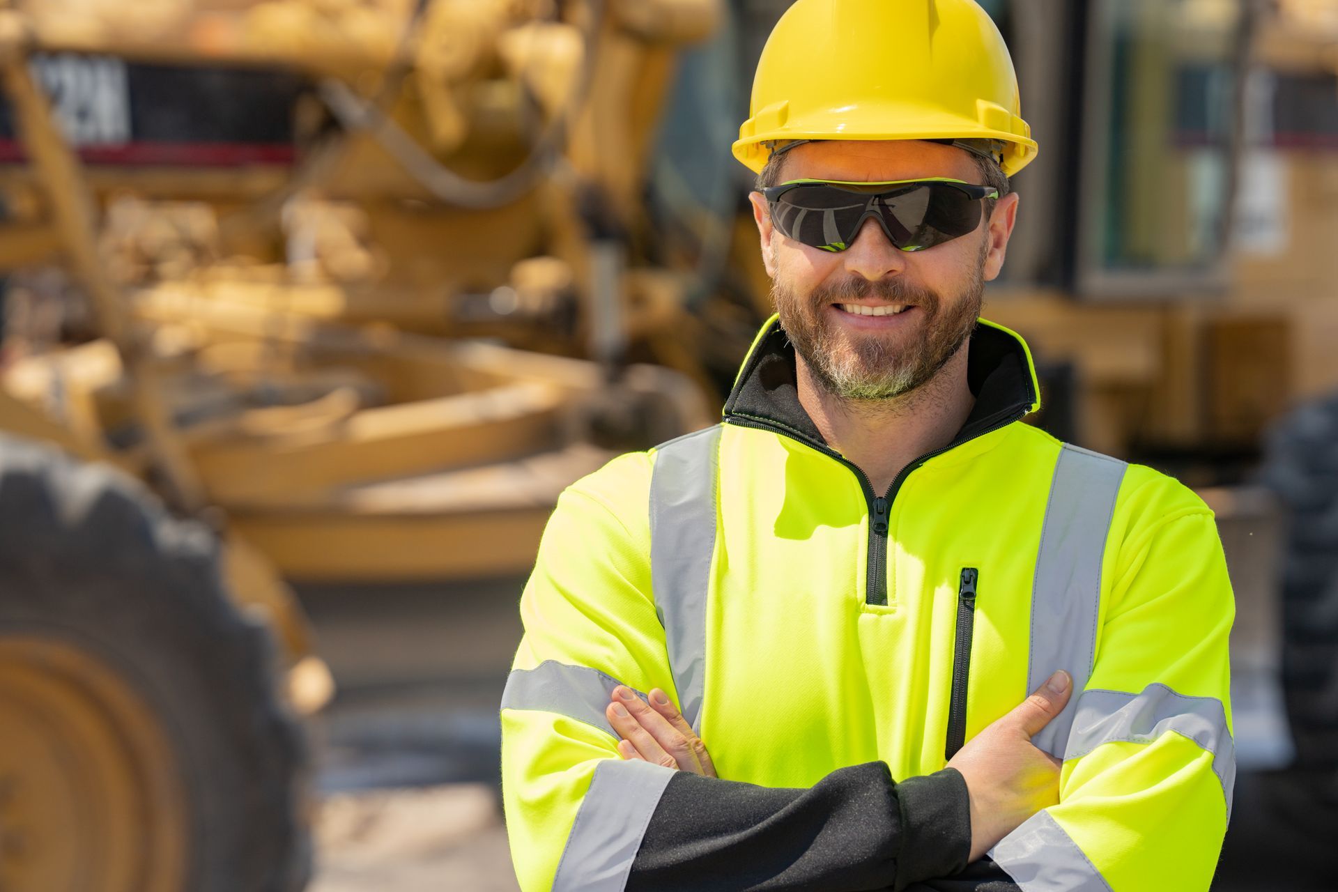 A construction worker wearing a hard hat and sunglasses is standing in front of a bulldozer.