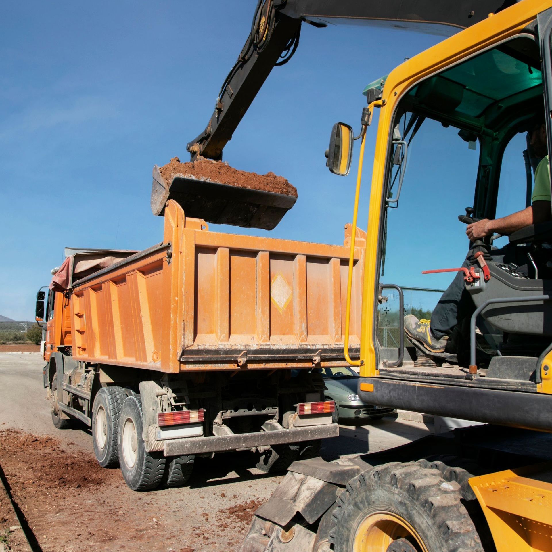 A dump truck is being loaded with dirt by a yellow excavator