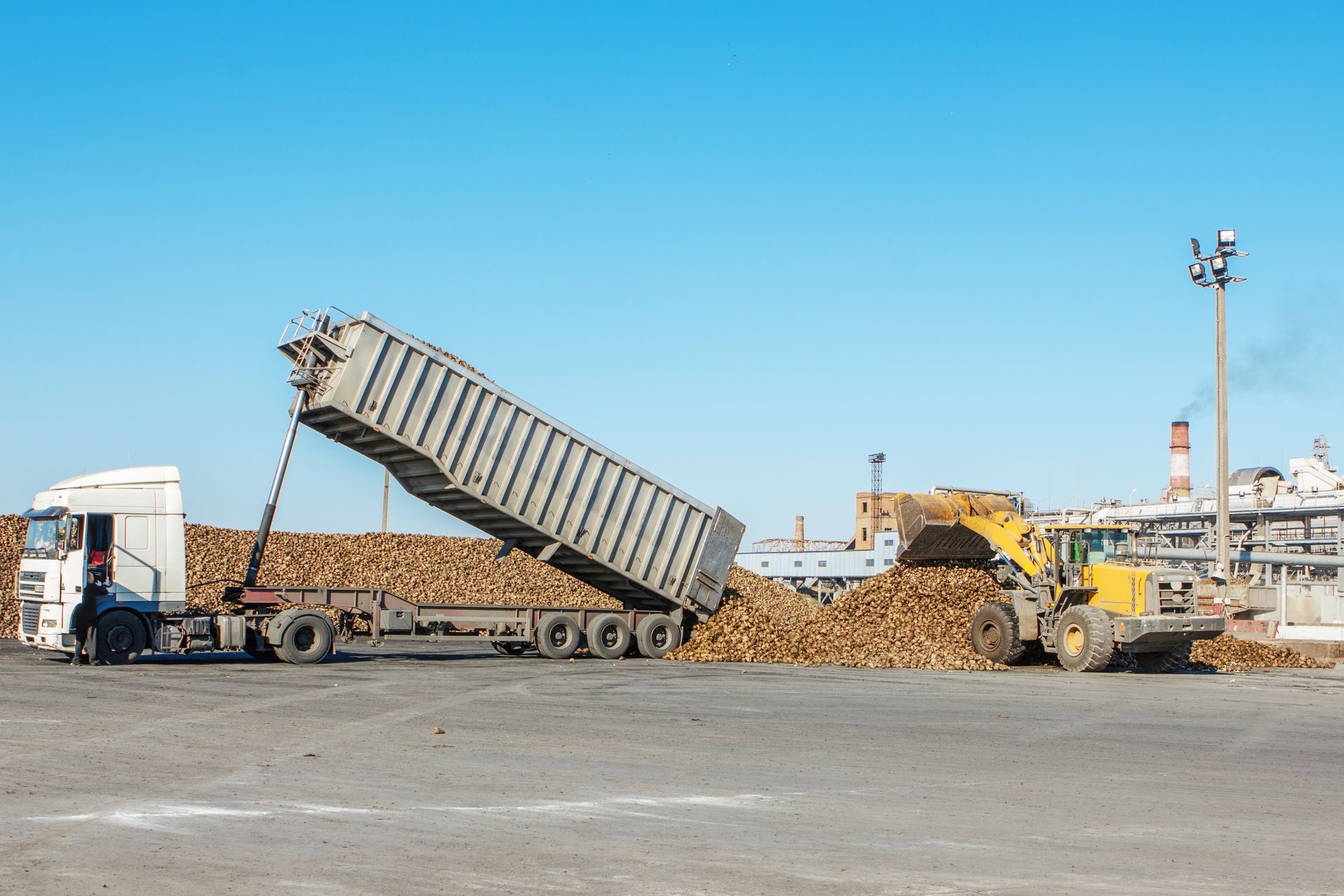 A dump truck is being loaded with wood in a parking lot.