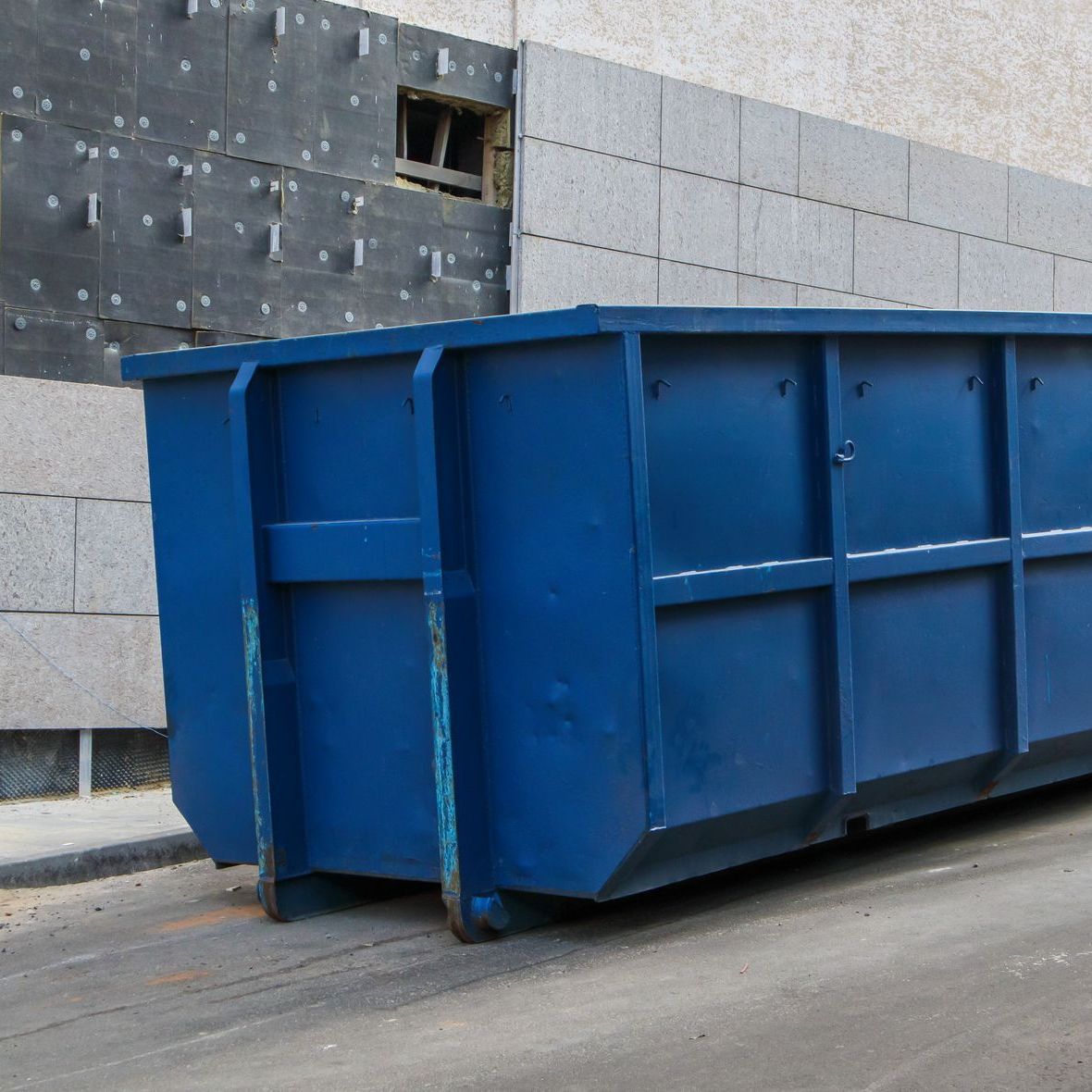 A large blue dumpster is parked in front of a building