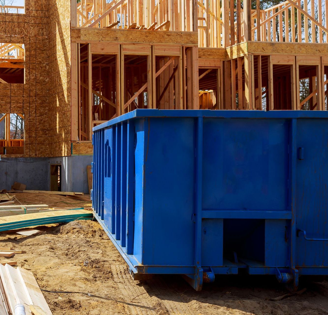 A blue dumpster is in front of a house under construction
