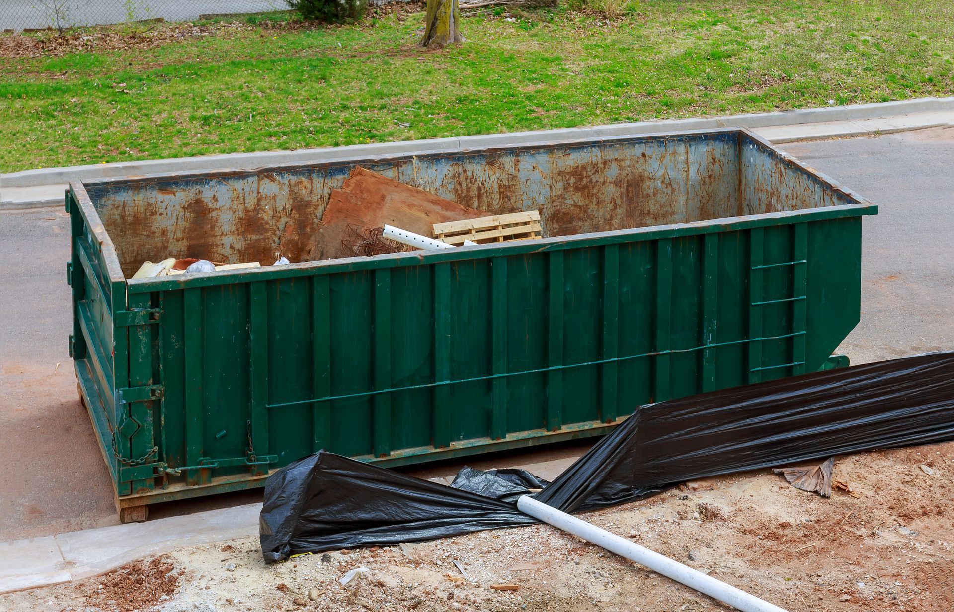 A green dumpster is sitting on the side of the road.
