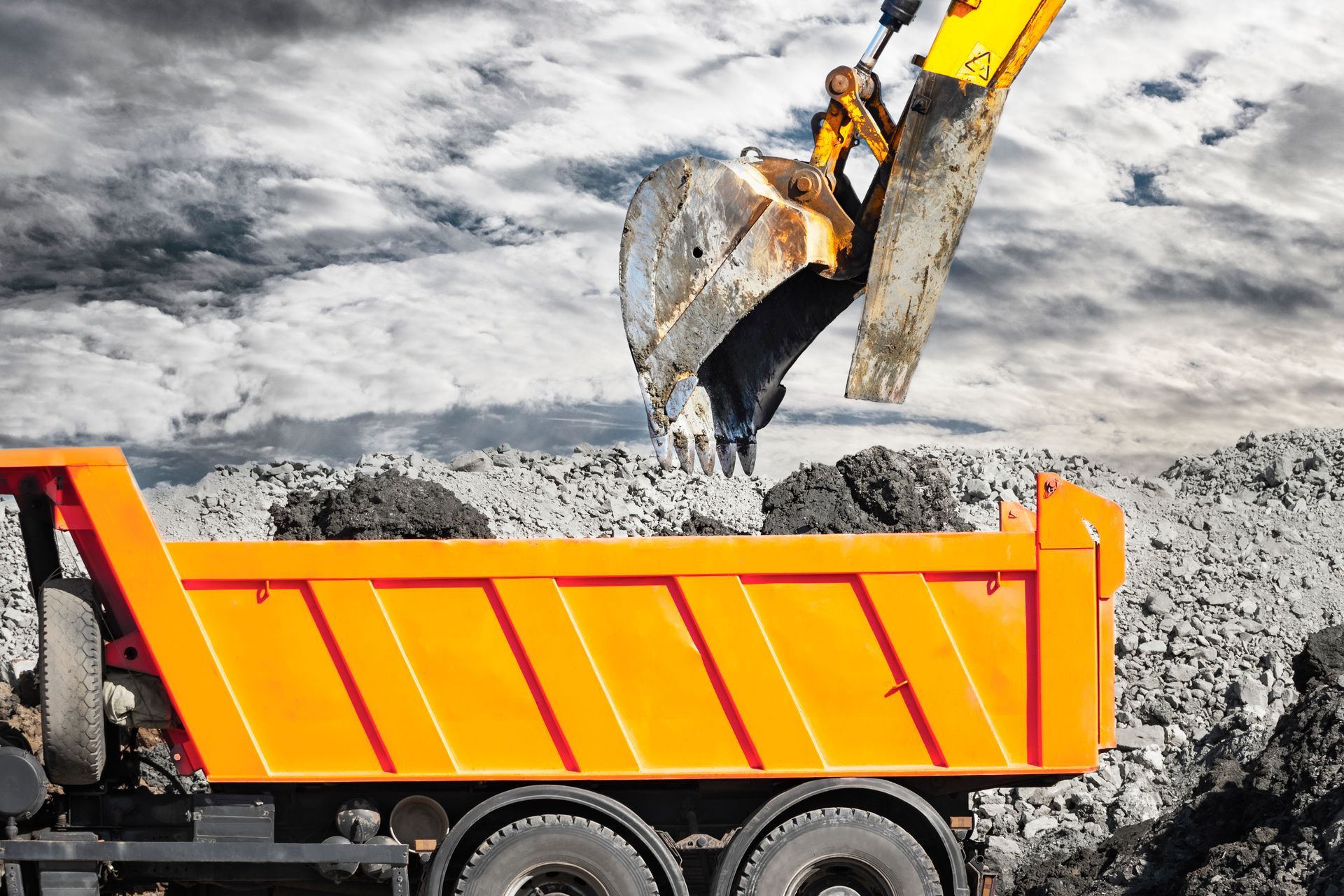 A dump truck is being loaded with dirt by an excavator.