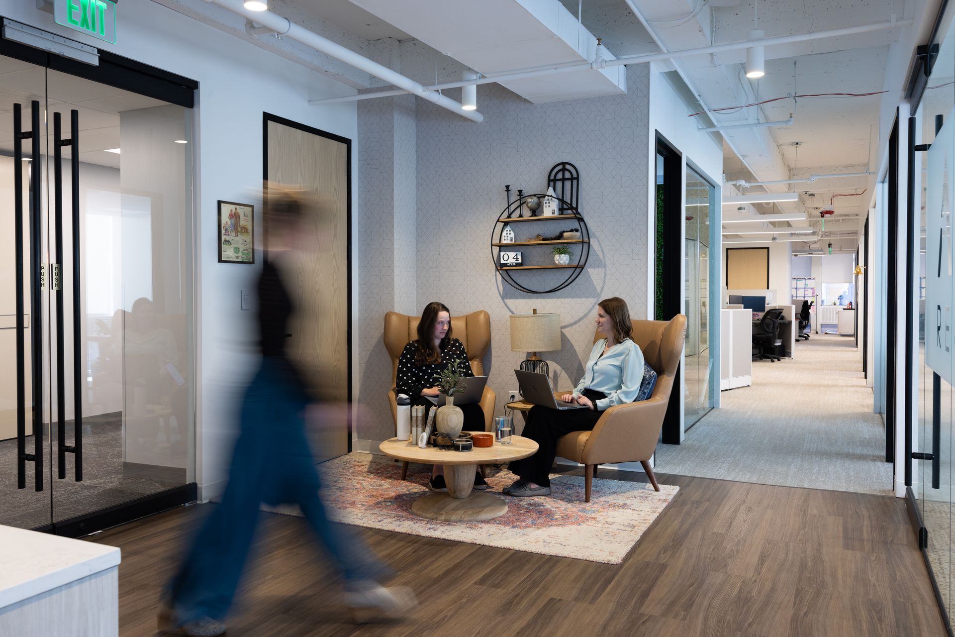 Two women are sitting at a table in an office talking to each other.