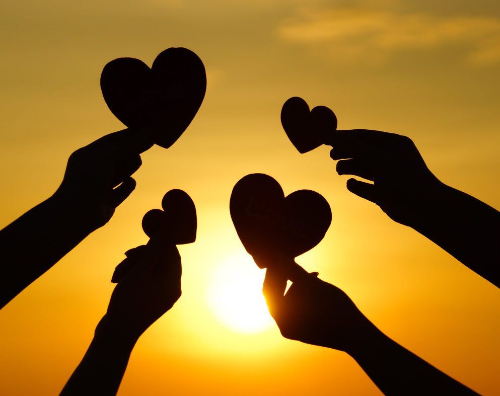 A group of people holding hearts in front of the sun