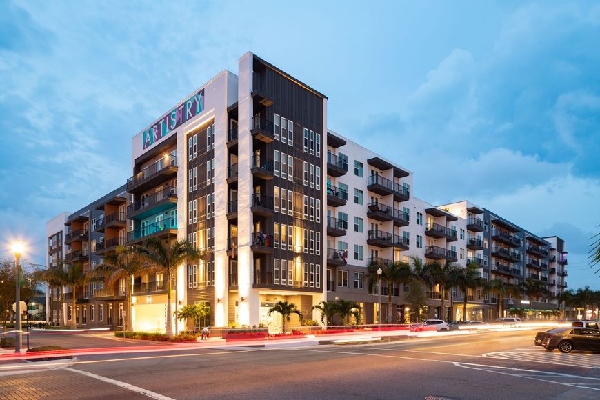 A large apartment building is sitting on the corner of a city street. Arte St Pete