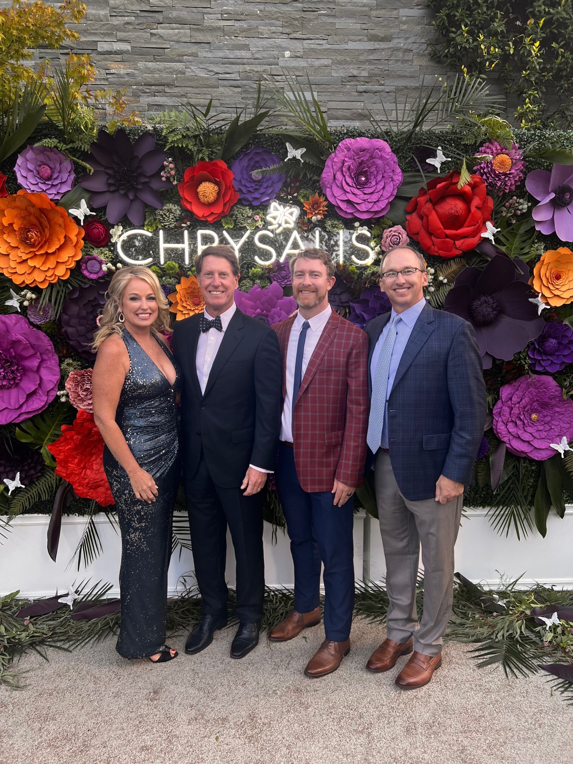 A group of people standing in front of a wall of flowers.