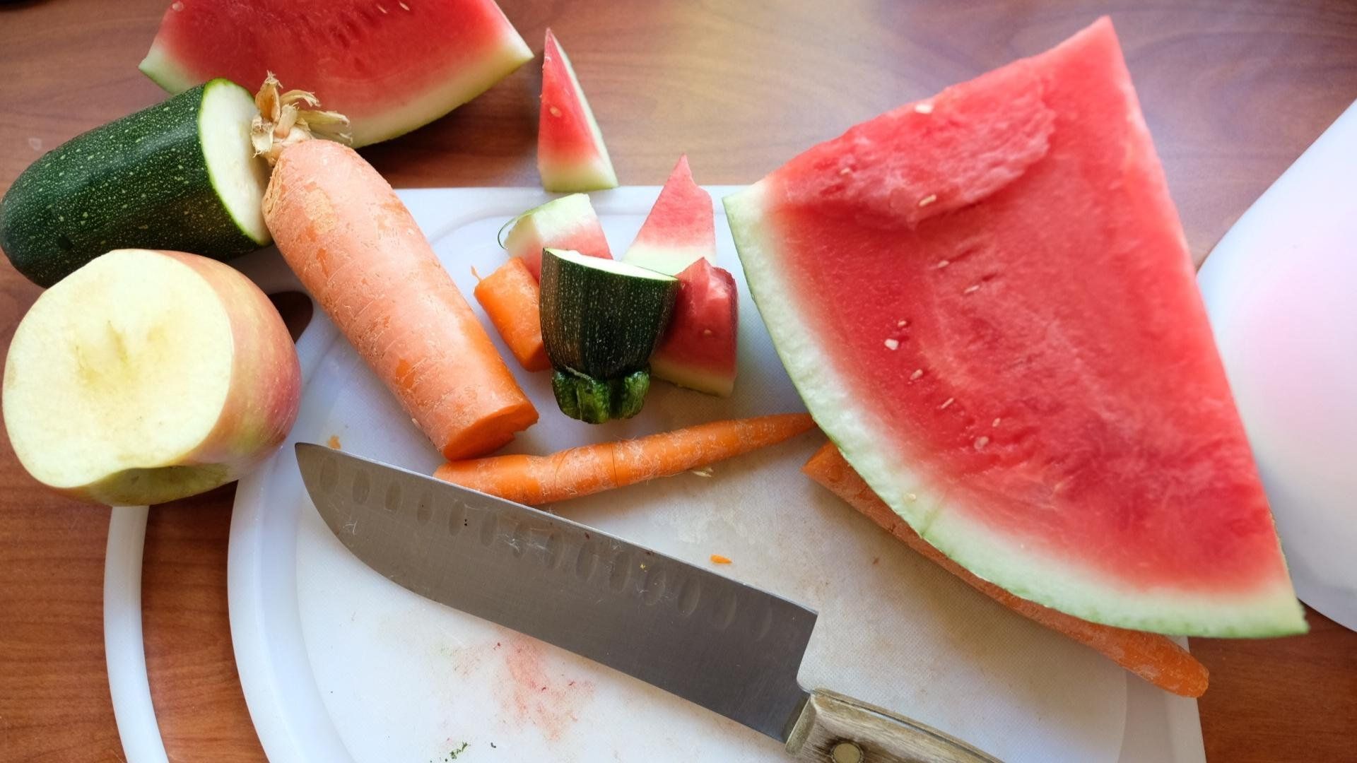 A cutting board with watermelon carrots and apples on it