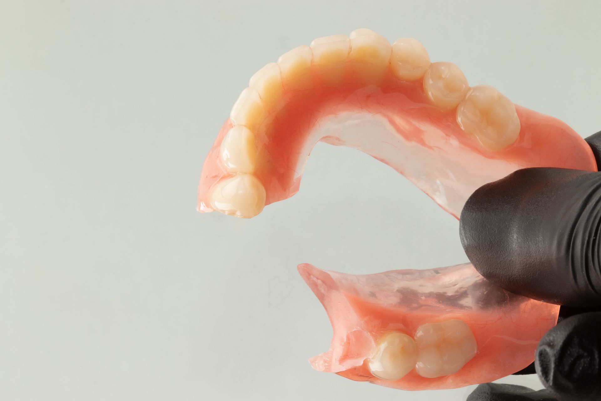 Gloved hand holding upper and lower pink dentures with white teeth on a light background Gloved hand holding upper and lower pink dentures with white teeth on a light background