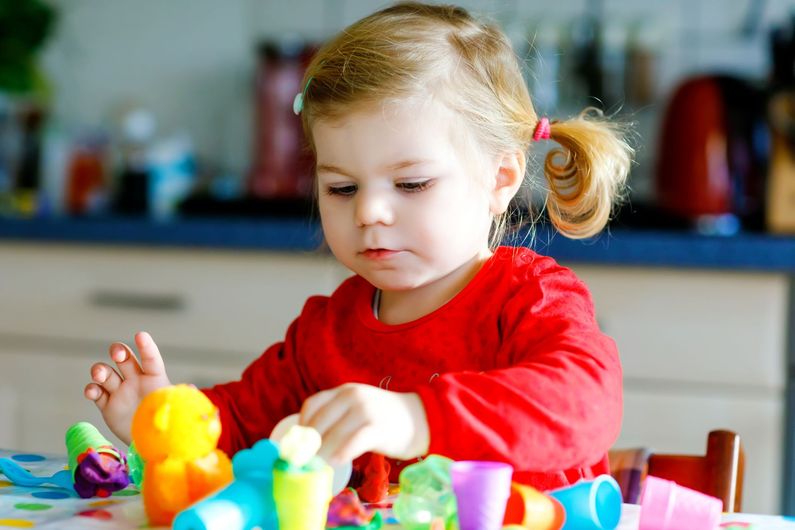 Child in a red shirt playing with colorful toys at a table