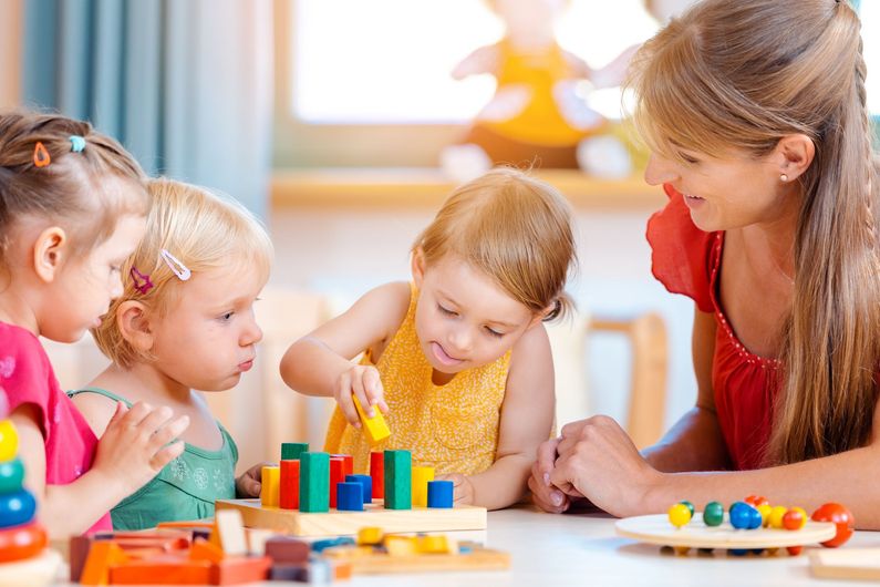Children playing with colorful blocks at a table with an adult in a bright classroom