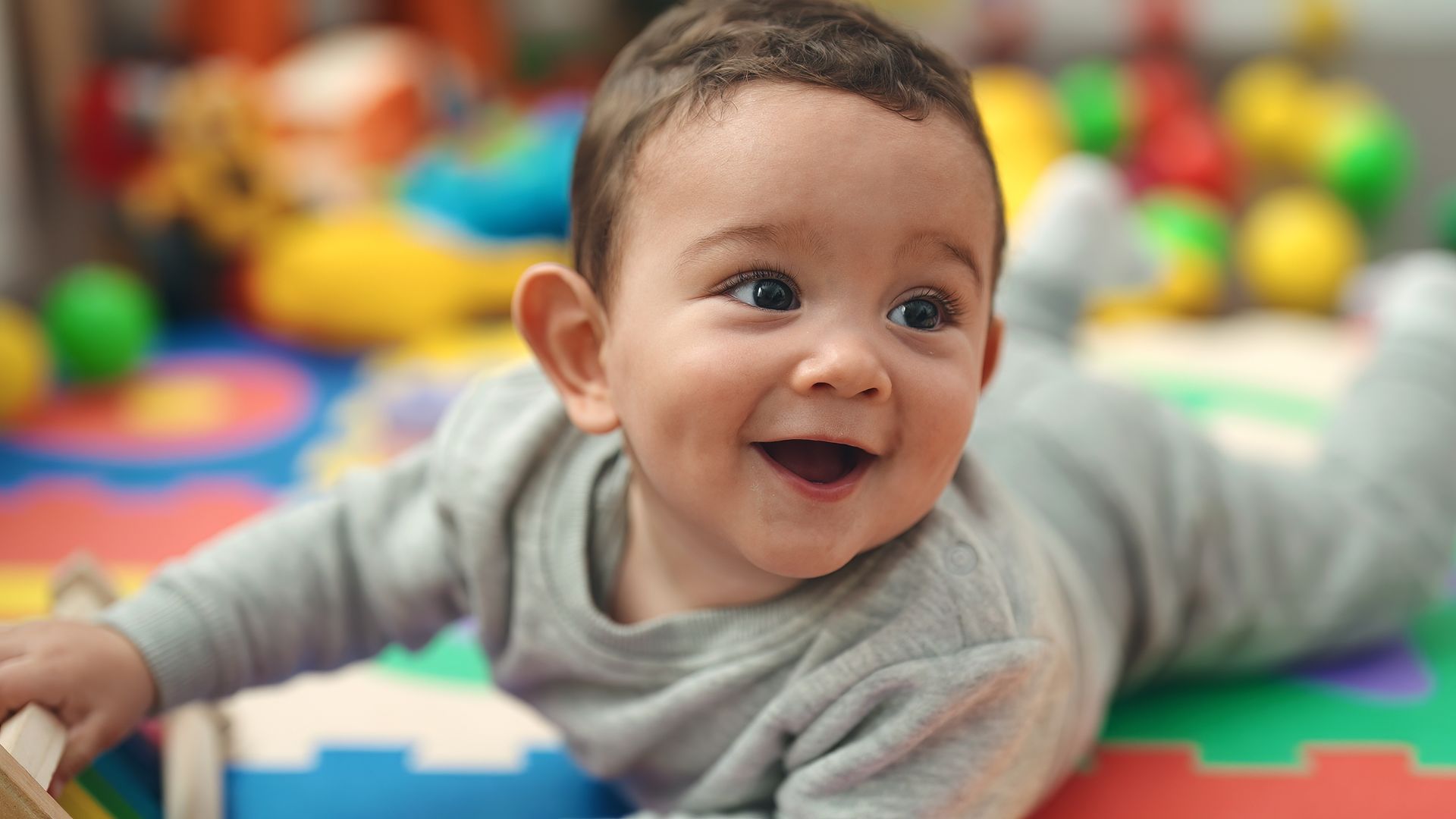 Smiling baby lying on a colorful foam play mat, arms outstretched.
