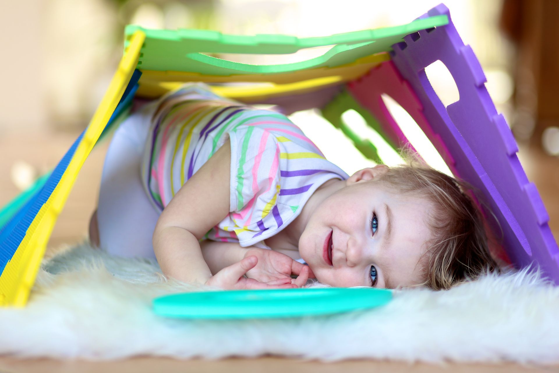 Child smiling inside a colorful cardboard fort on a fluffy white blanket Child smiling inside a colorful cardboard fort on a fluffy white blanket