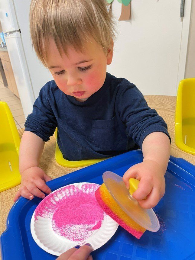 Child playing with colorful plates at a table, holding a yellow lid and looking down. Child playing with colorful plates at a table, holding a yellow lid and looking down.