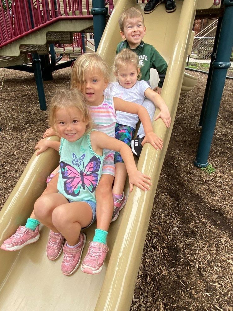 Four children sitting one behind another on a playground slide, smiling Four children sitting one behind another on a playground slide, smiling
