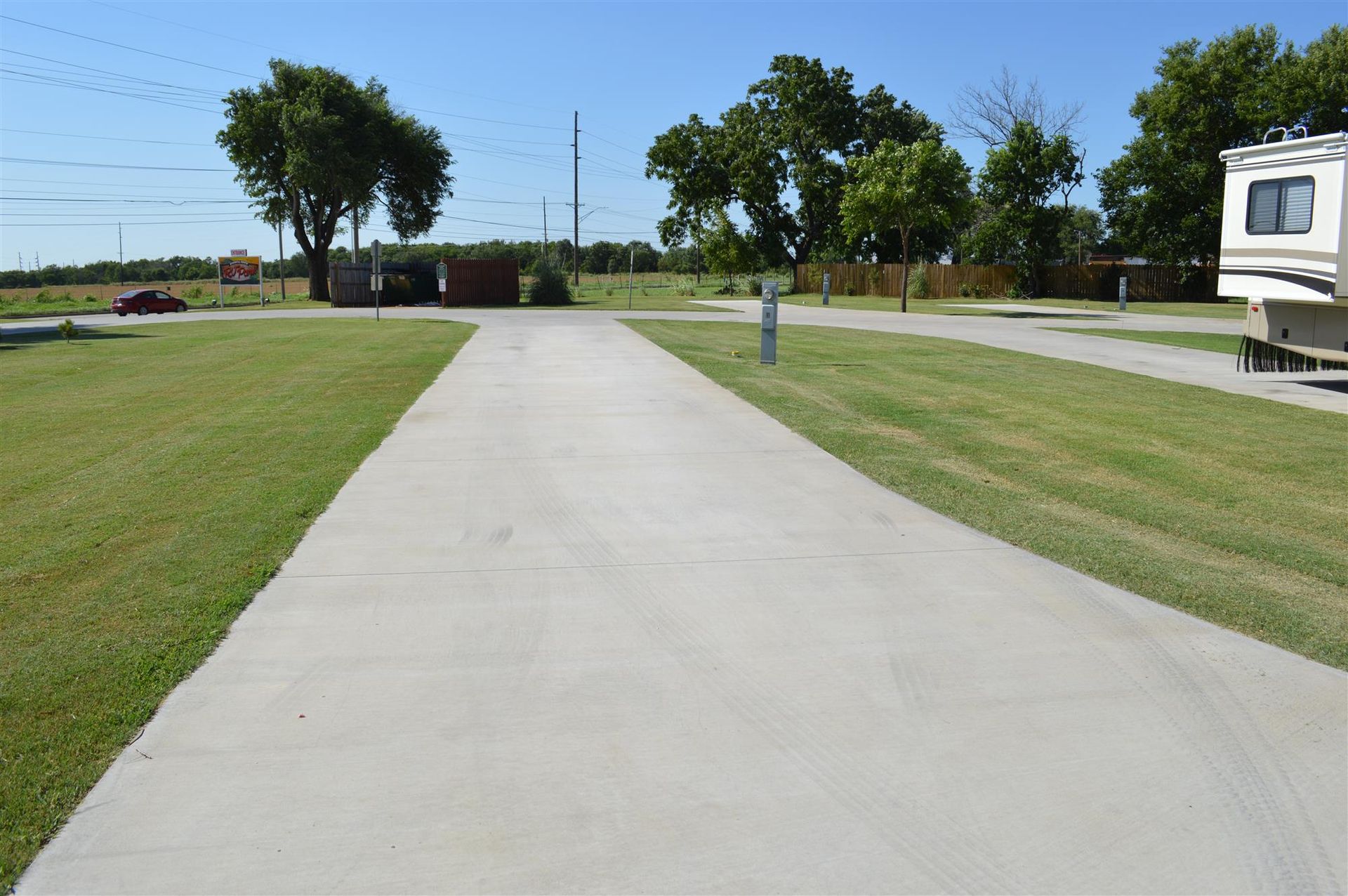 Paved path through a grassy park under a clear blue sky, with trees and an RV on the right