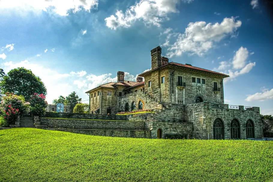 Stone farmhouse with arched walls on a green field under a bright blue sky with clouds