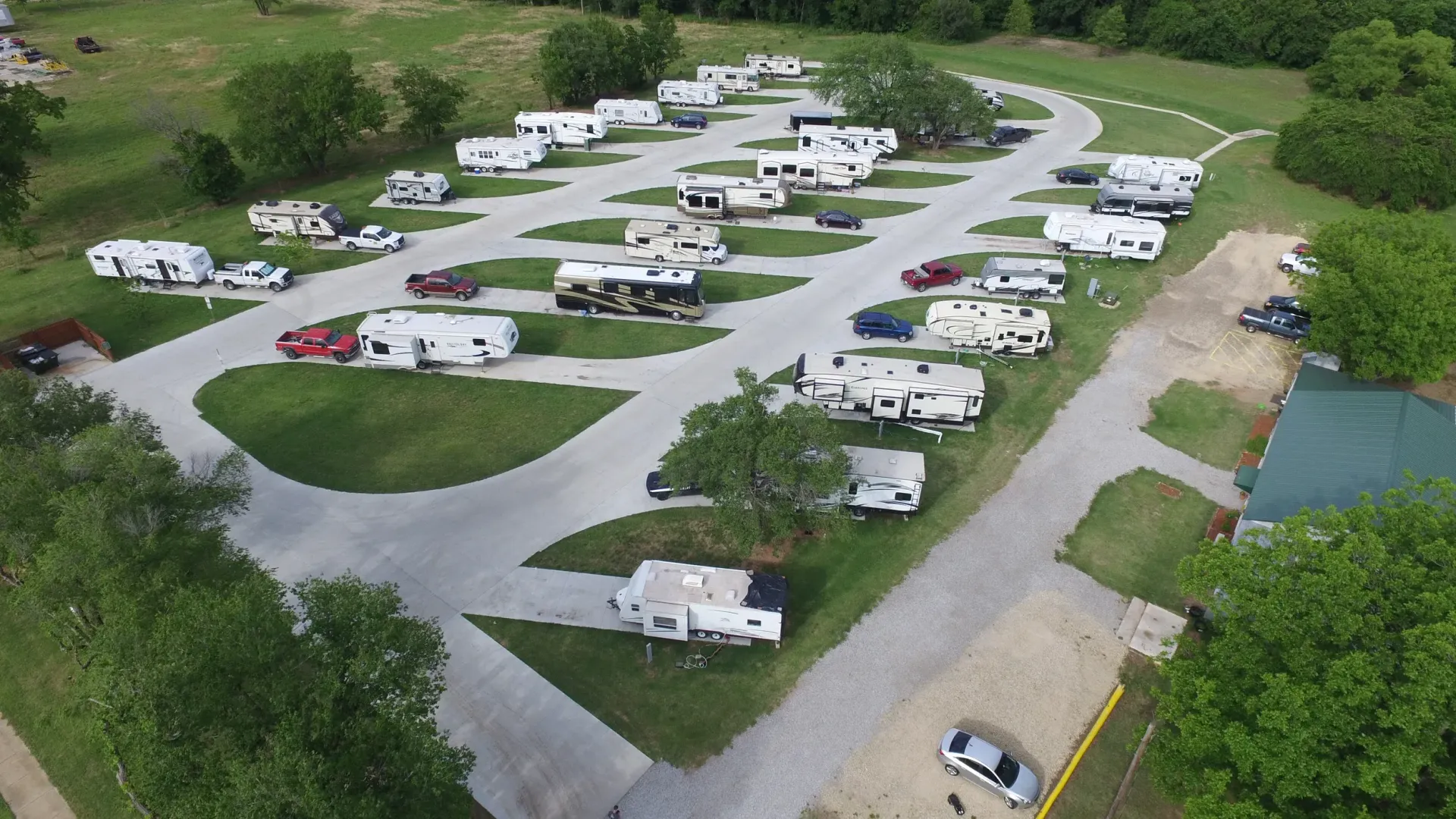 Aerial view of a campground with many RVs and trailers parked on paved loops near grass and a small pond.