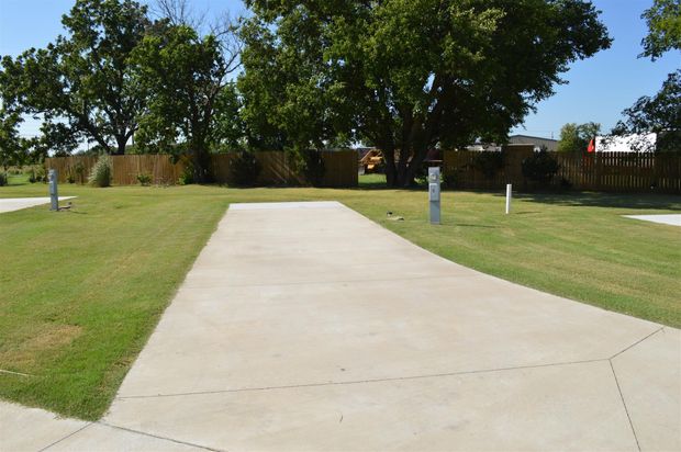 Concrete sidewalk leading through a grassy park with trees and white posts
