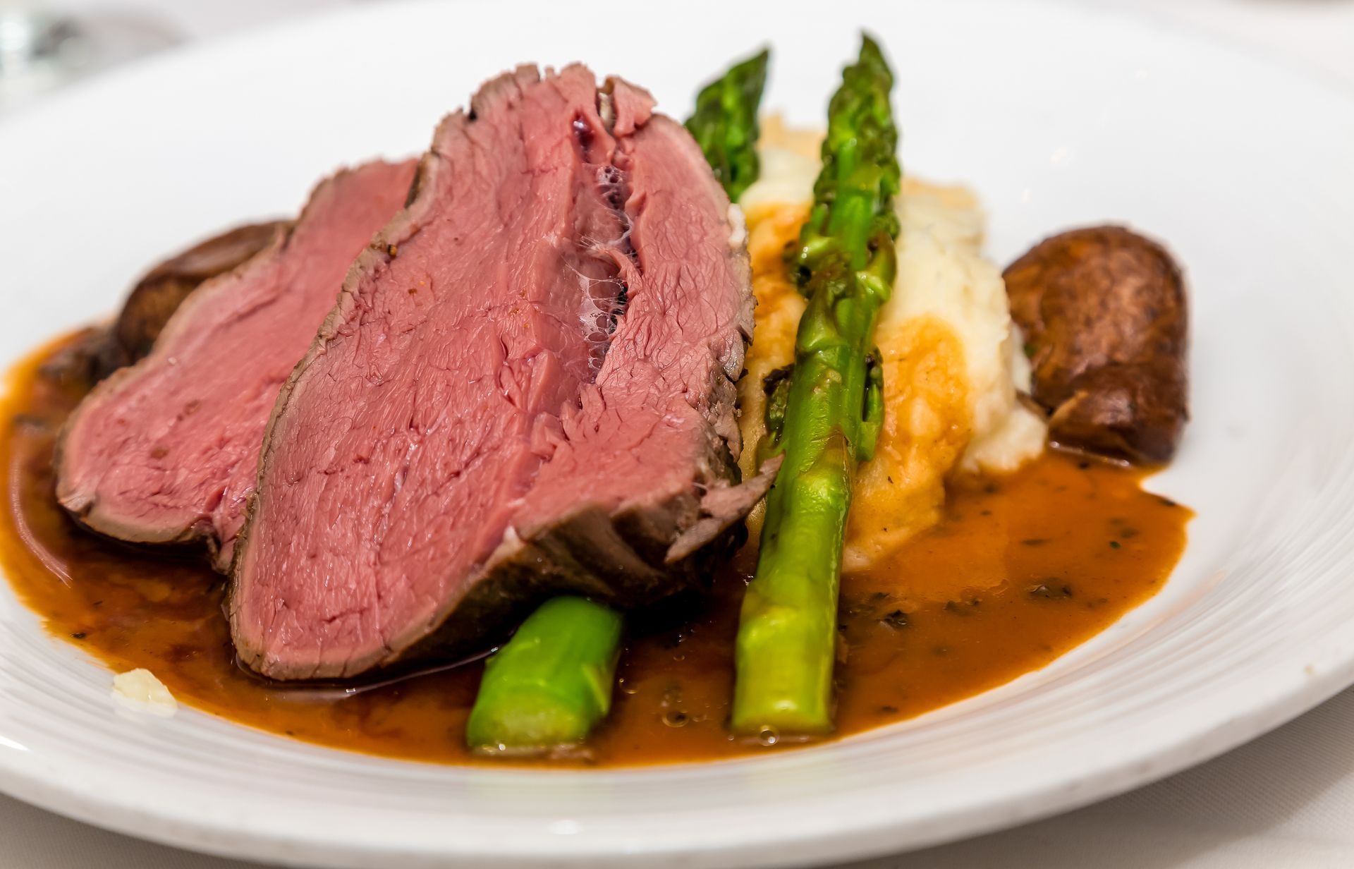 Sliced medium-rare steak with asparagus and sauce on a white plate