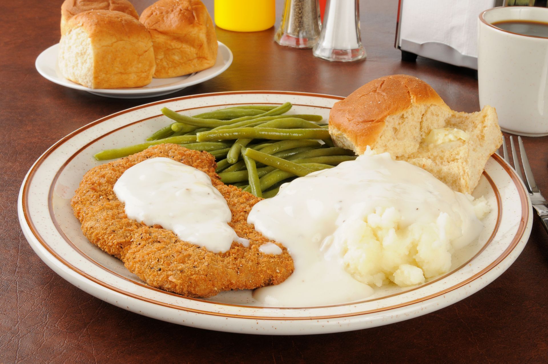 Breaded chicken cutlet with gravy, mashed potatoes, green beans, and a dinner roll on a plate