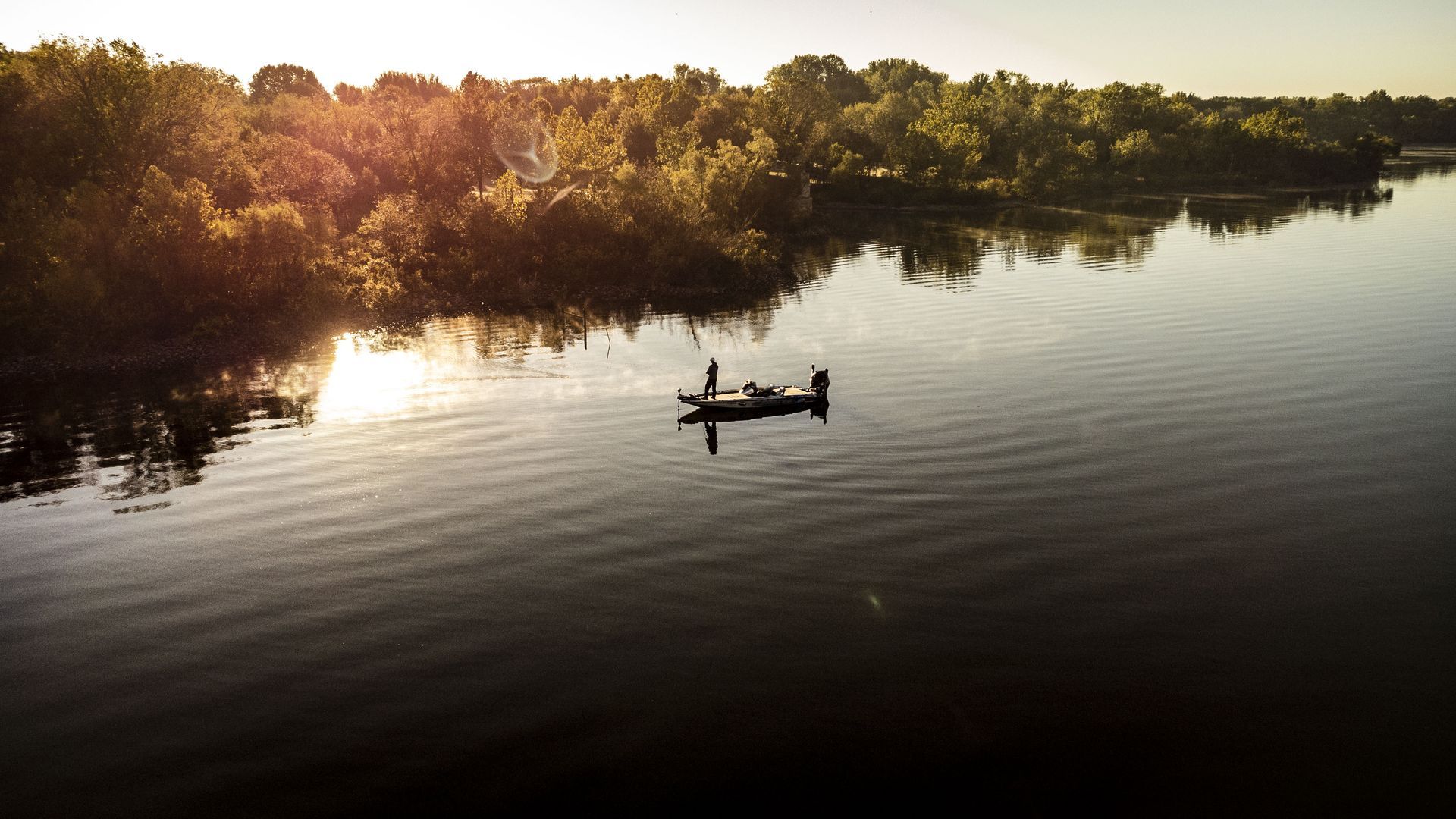 Small boat on a calm river at sunset, with trees reflecting on the water.