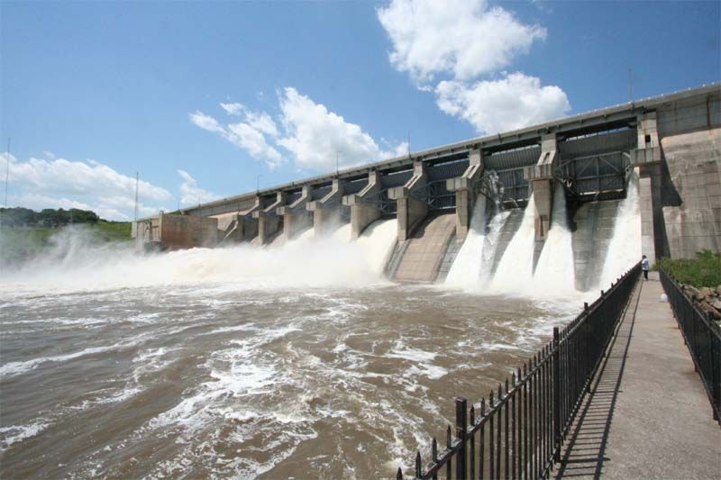 Concrete dam releasing roaring white water under a blue sky