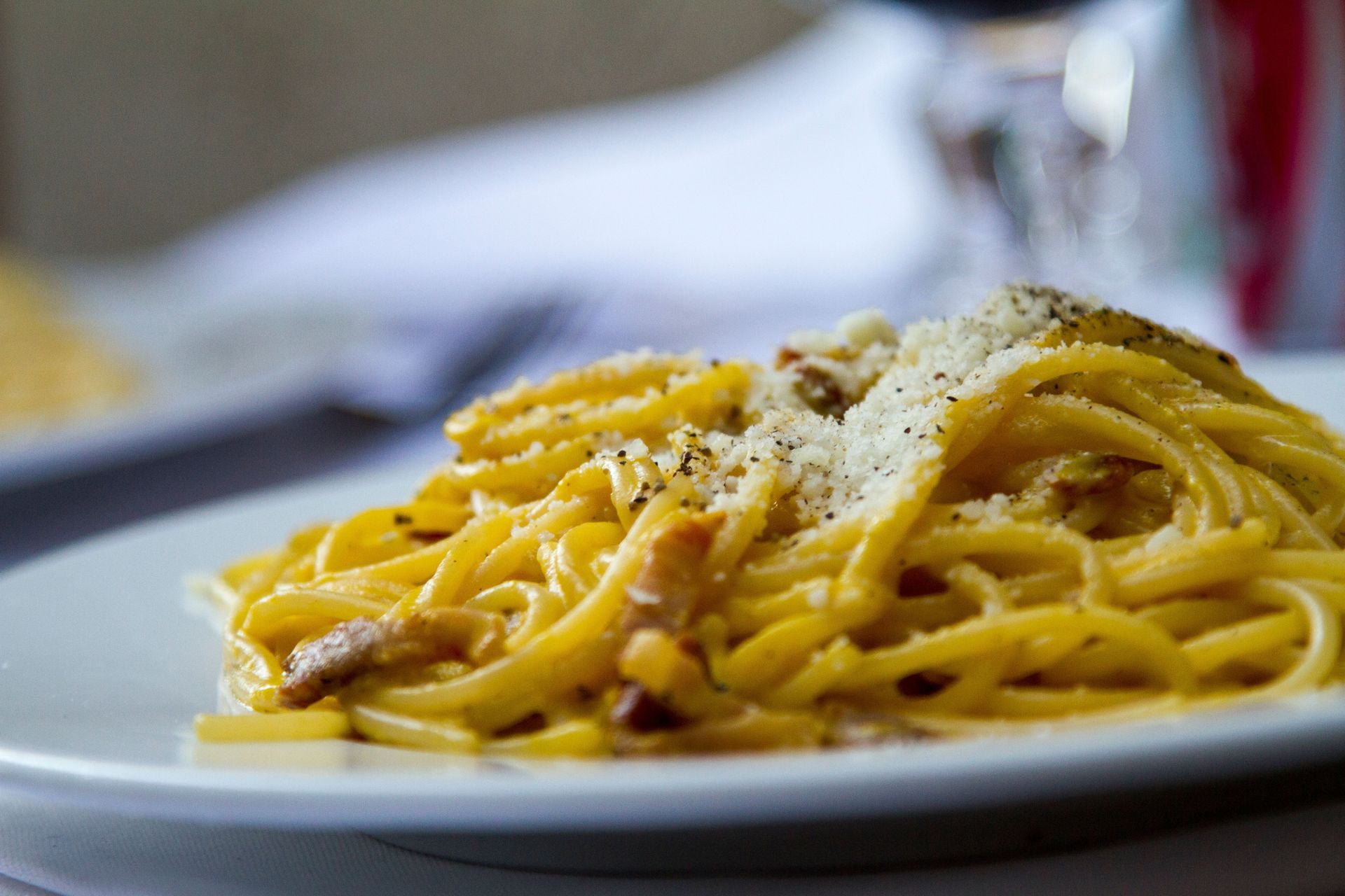 Plate of spaghetti with grated cheese and pepper, served on a white dish
