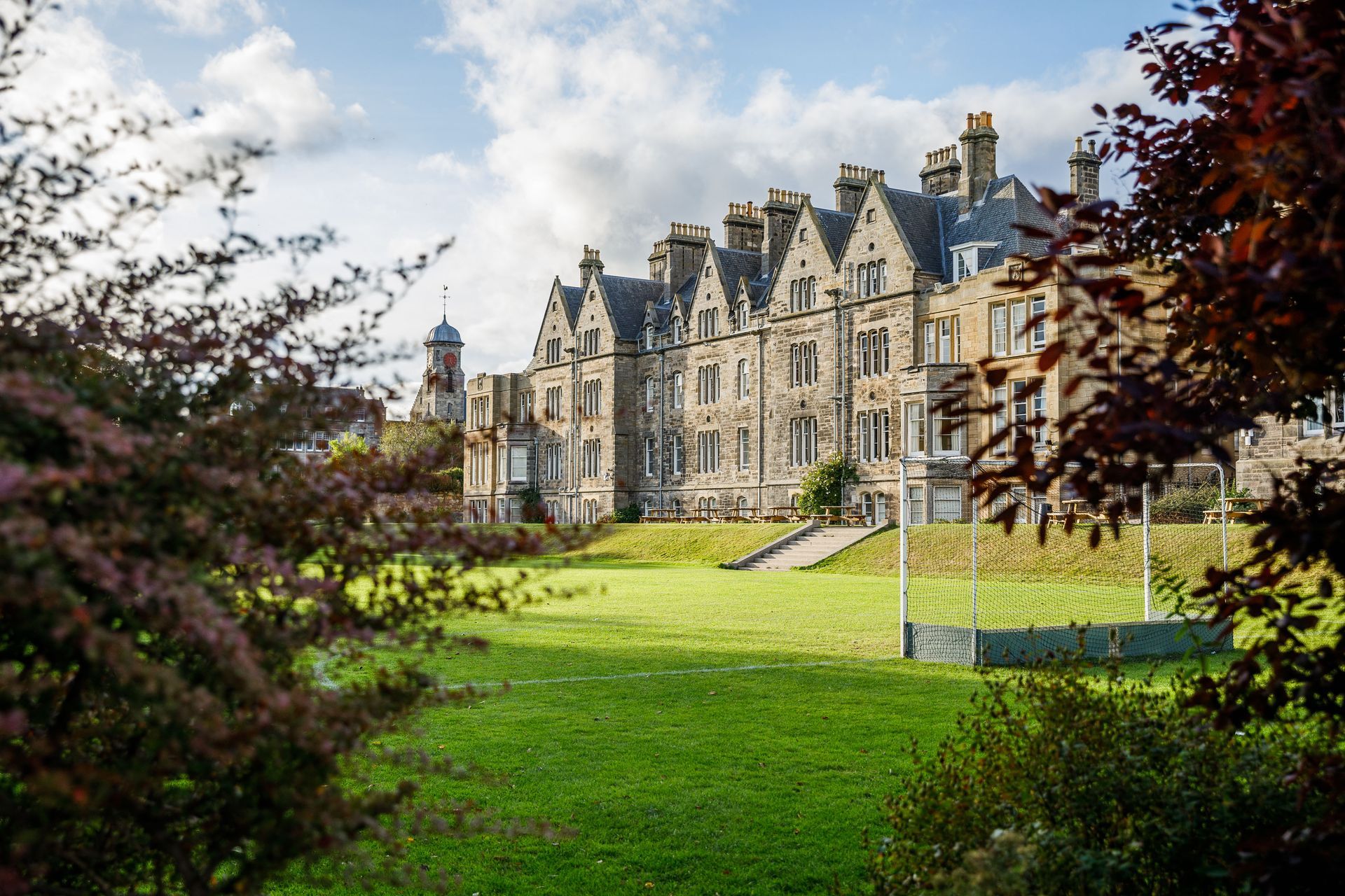 Stone manor with manicured lawn and pink roses in the foreground under a blue sky