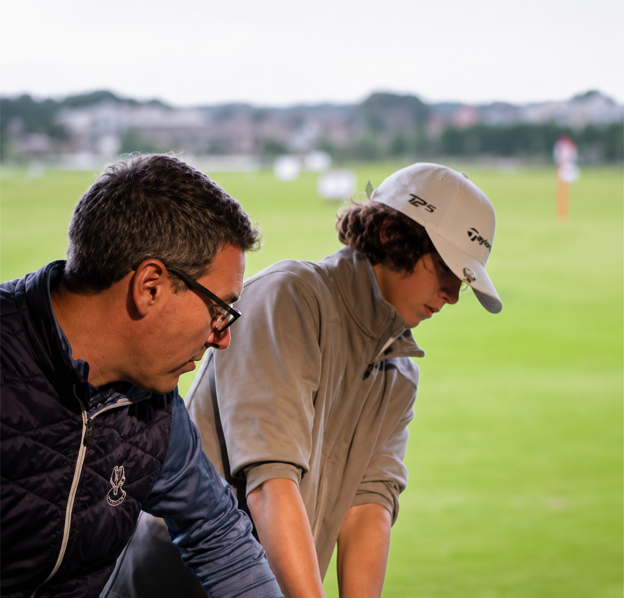 Golfer practicing a putt indoors, aiming at a ball near a tray of yellow golf balls.