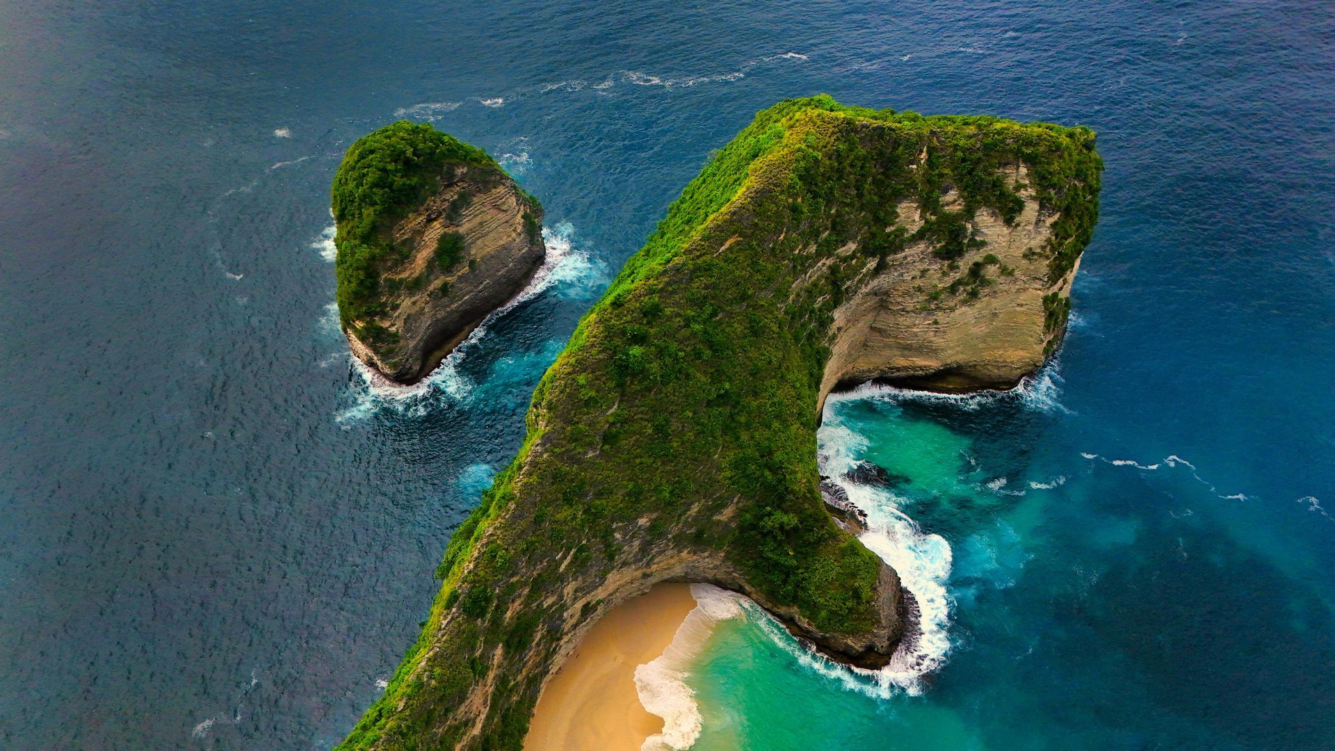 Aerial view of a tropical island with green cliffs, blue ocean, and a sandy beach