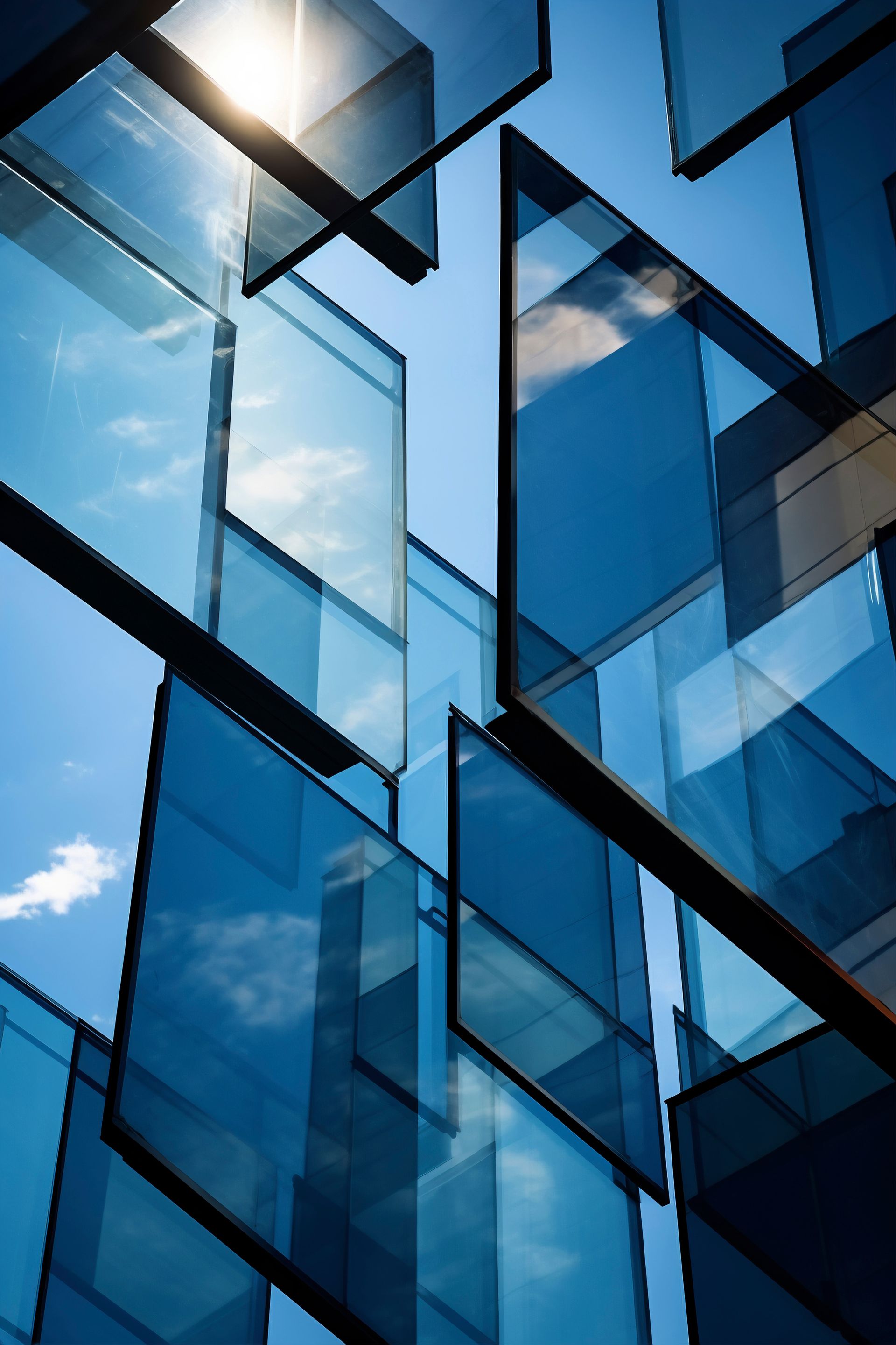 Gebouwgevel van blauw getint glas met reflecterende geometrische panelen en zonlicht