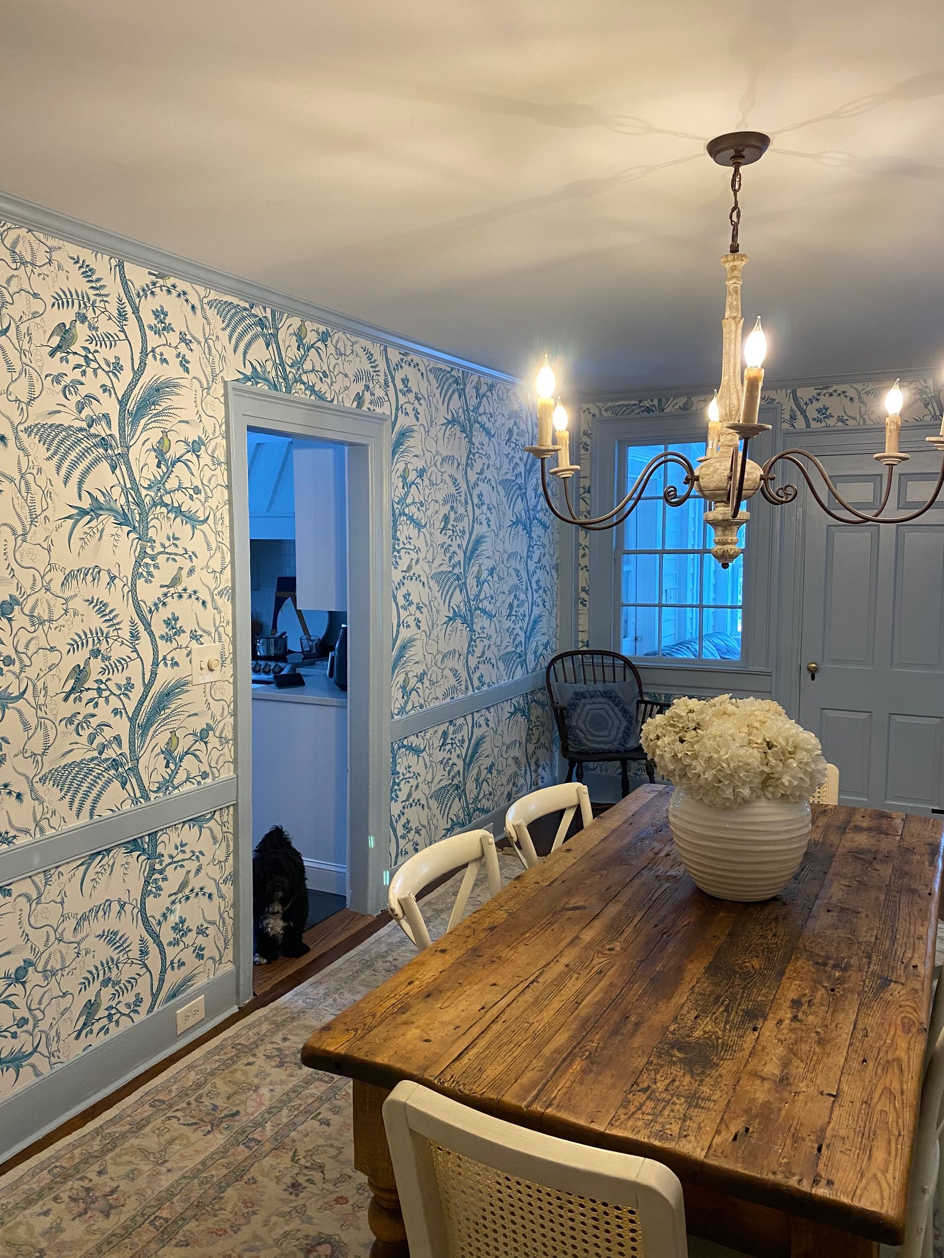A dining room with a wooden table and chairs and a chandelier hanging from the ceiling.