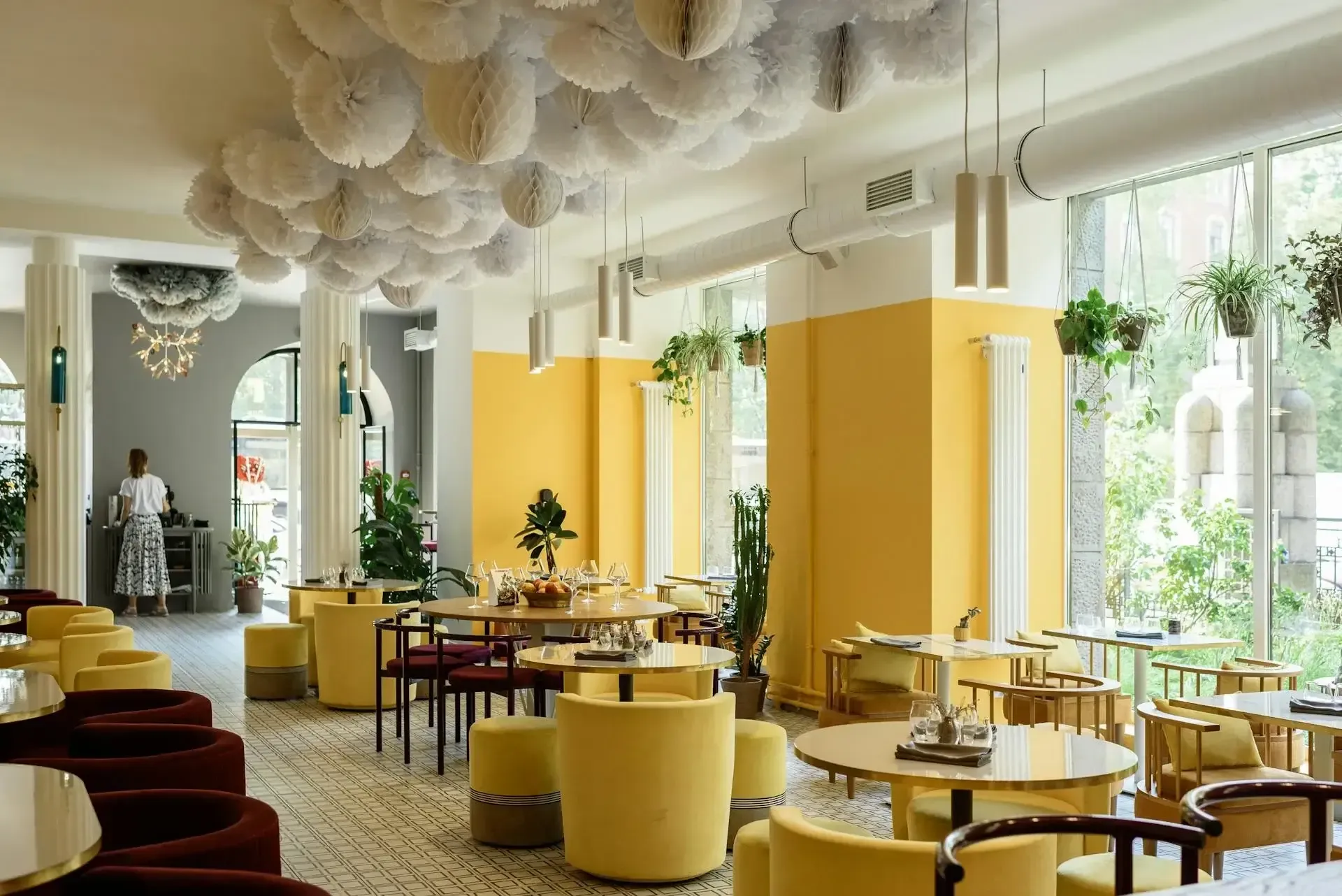 A restaurant with tables and chairs and a woman standing in the background.