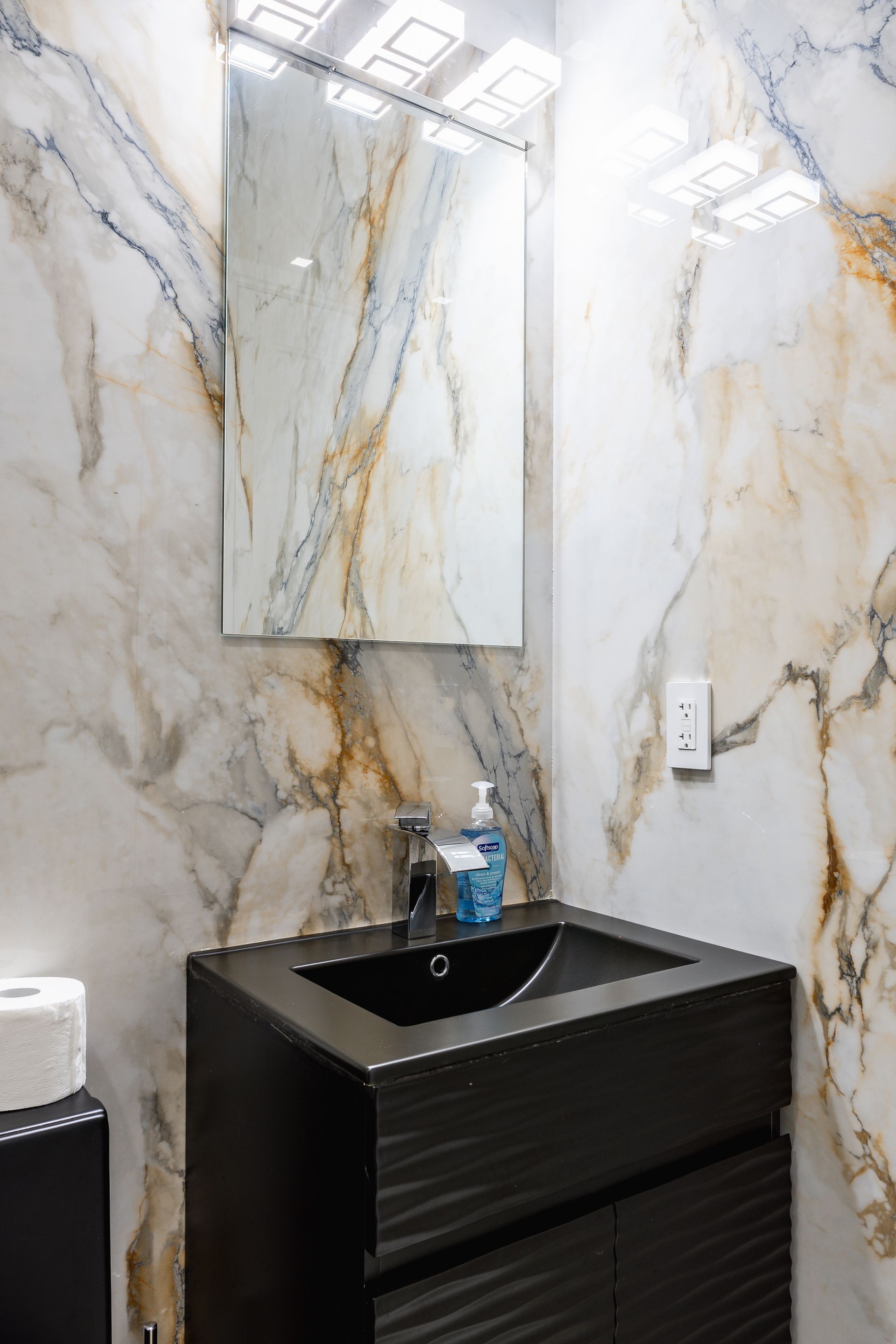 Bathroom with black vanity, sink, mirror, and marbled white and gold walls.