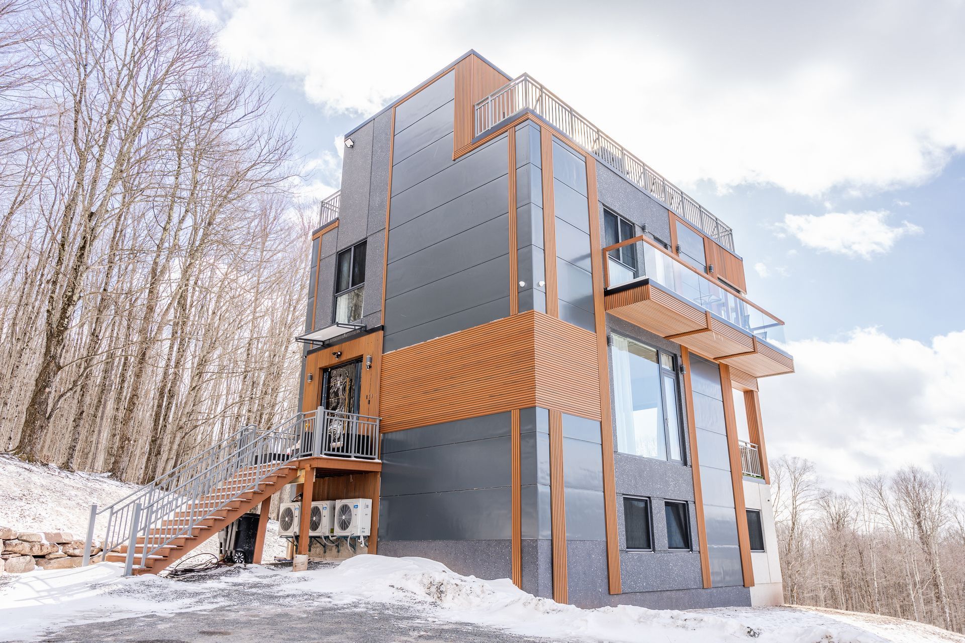Modern, multi-story building with gray siding, wooden accents, and glass balconies in a snowy outdoor setting.