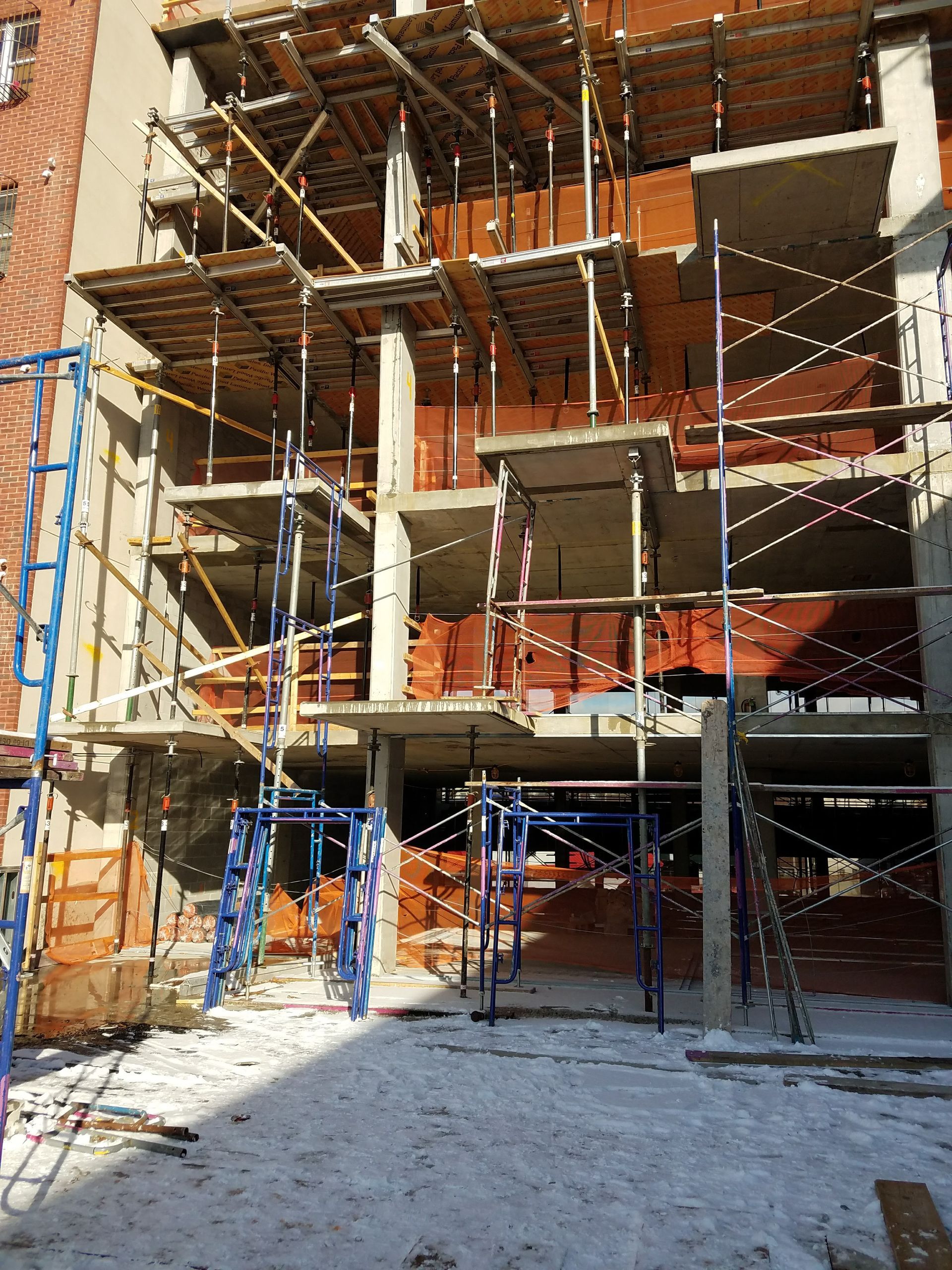 Building under construction, scaffolding surrounds concrete structure with exposed brickwork, outdoors in winter.