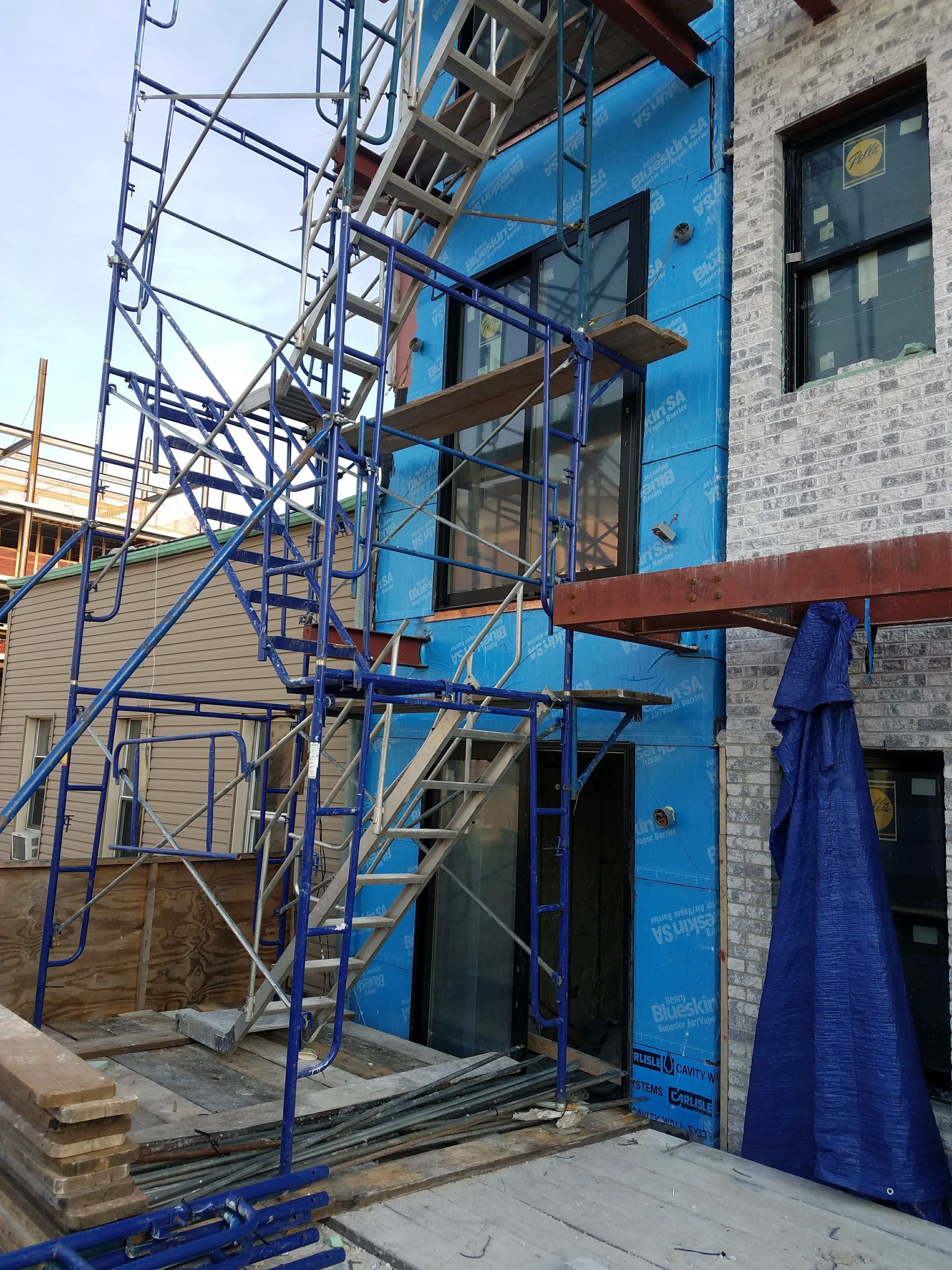 Scaffolding on building exterior under construction, with blue sheathing and brick facade.