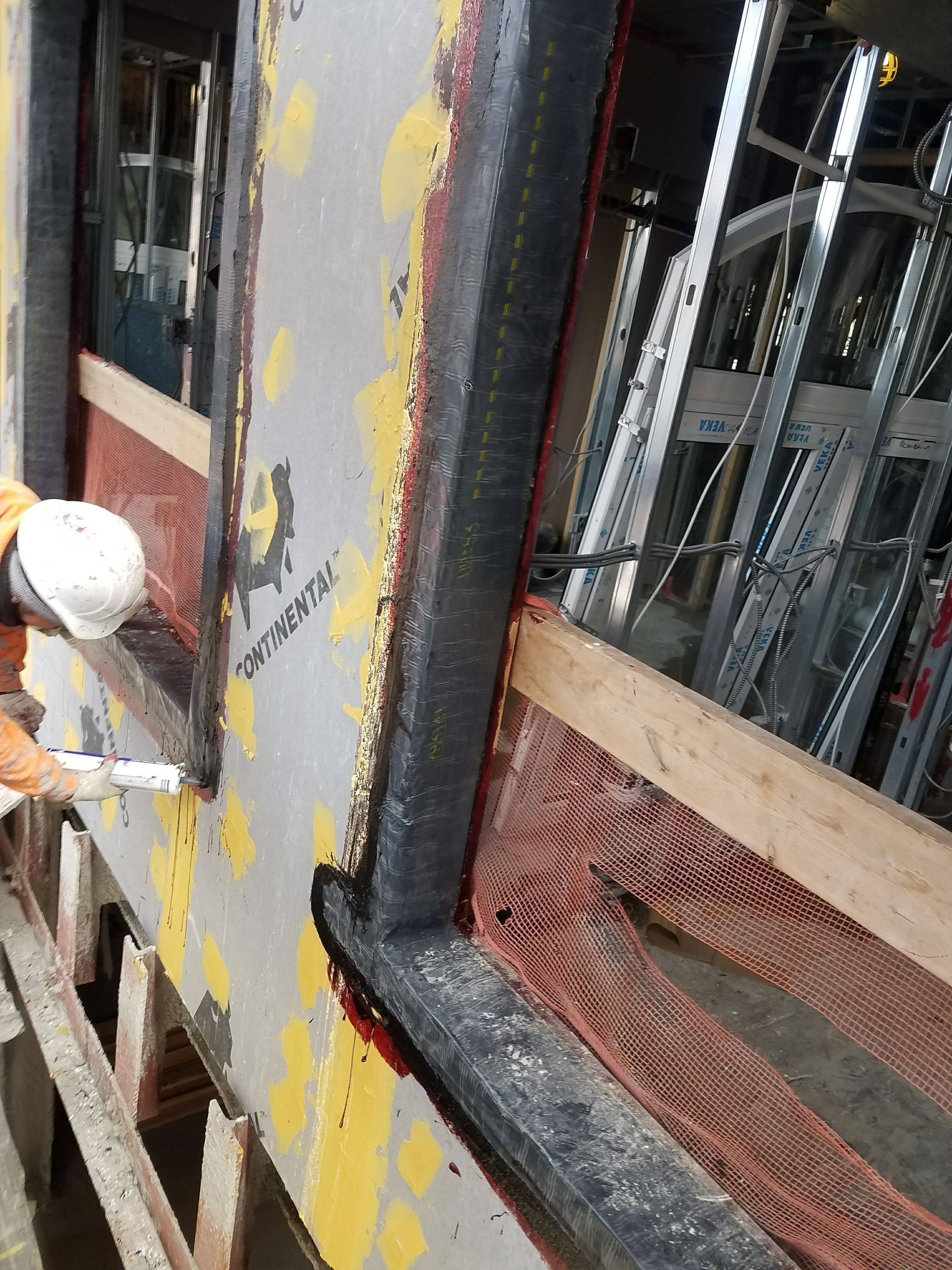 Person in hardhat caulking window frame during construction. Close-up of building exterior.