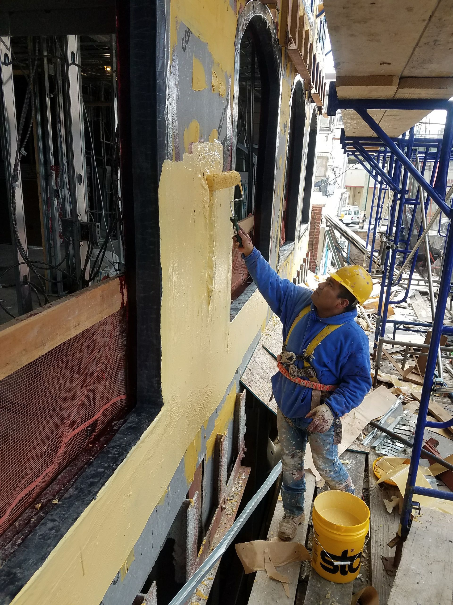 Construction worker applying yellow sealant on building facade.