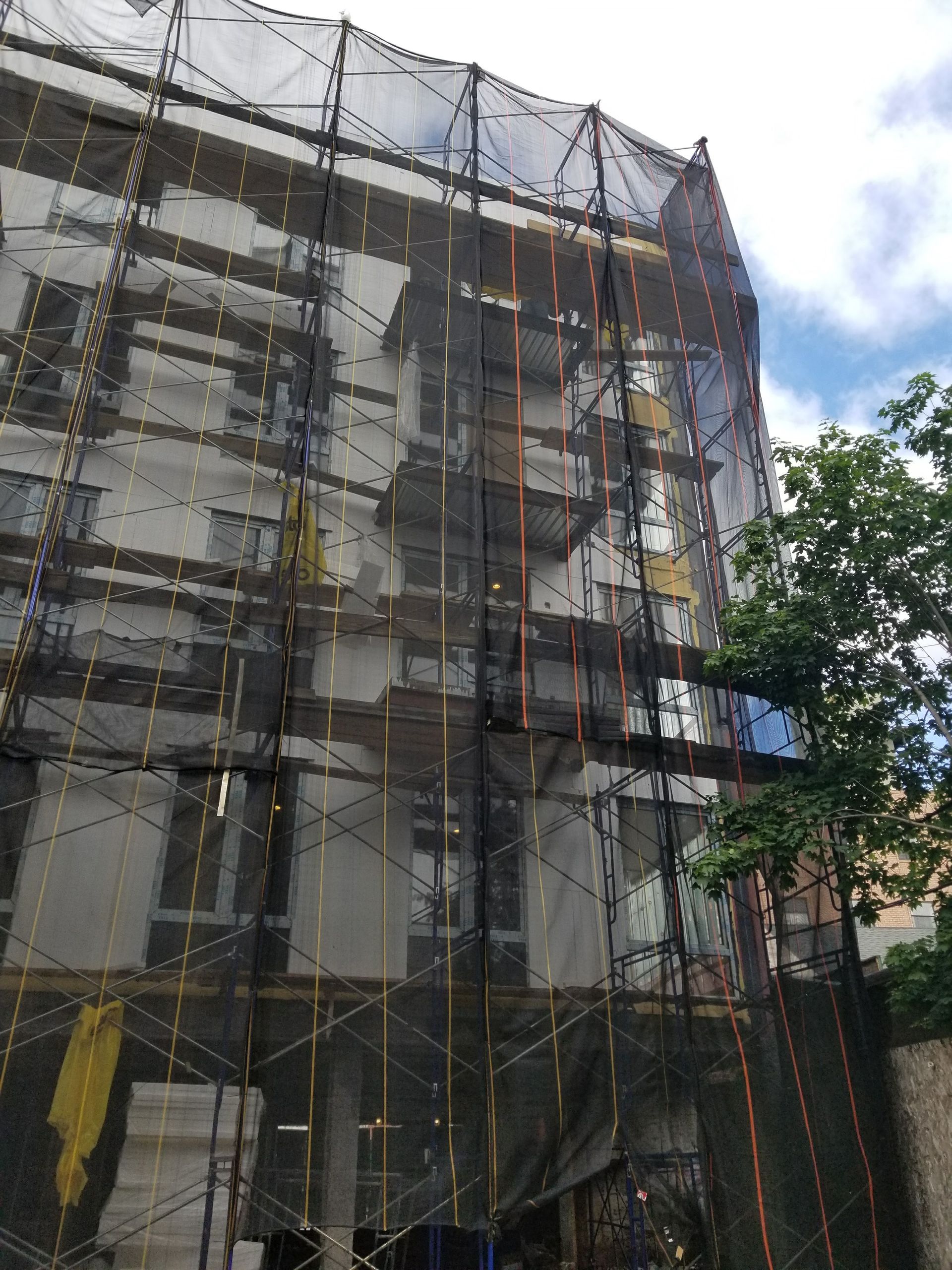 Building facade covered in black netting for construction, scaffolding visible.
