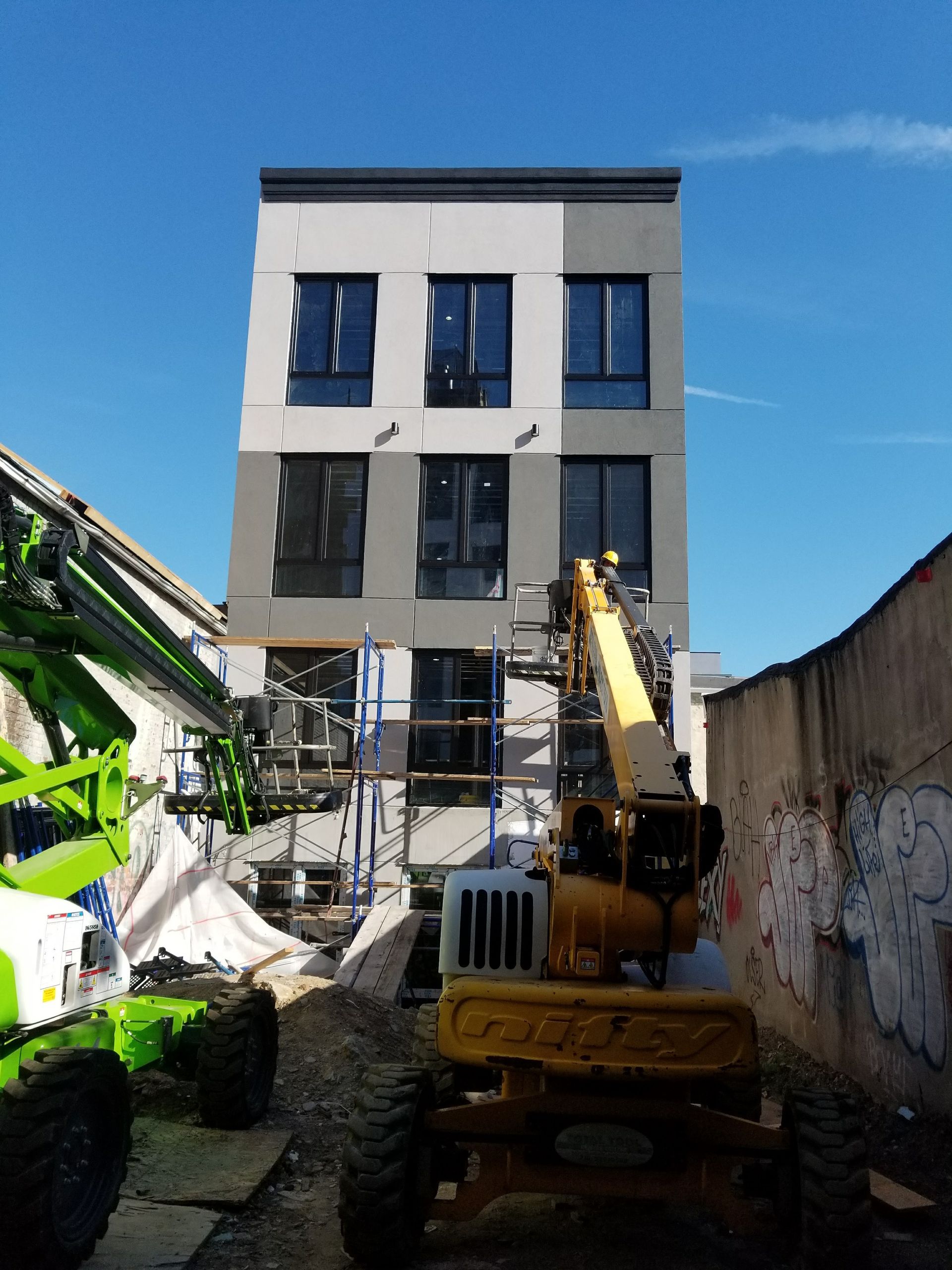 A multi-story building under construction, exterior view with a lift and scaffolding.
