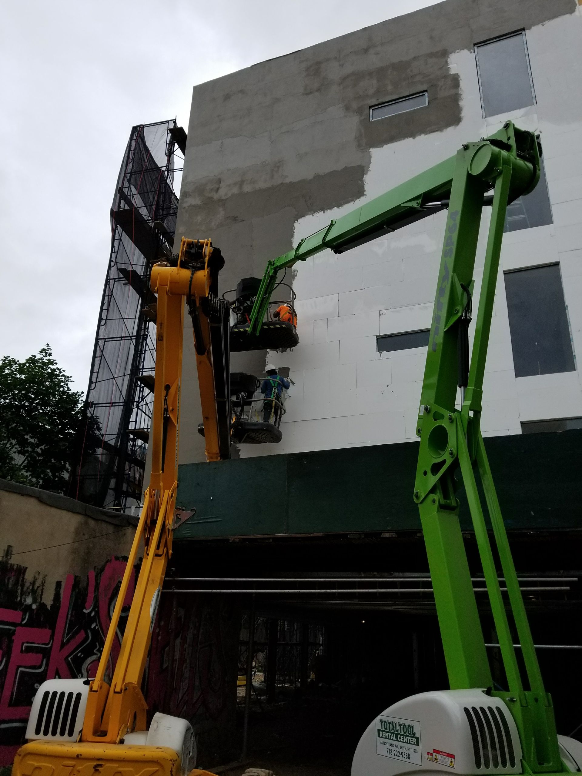 Two boom lifts at a building, workers on scaffolding and in lifts.
