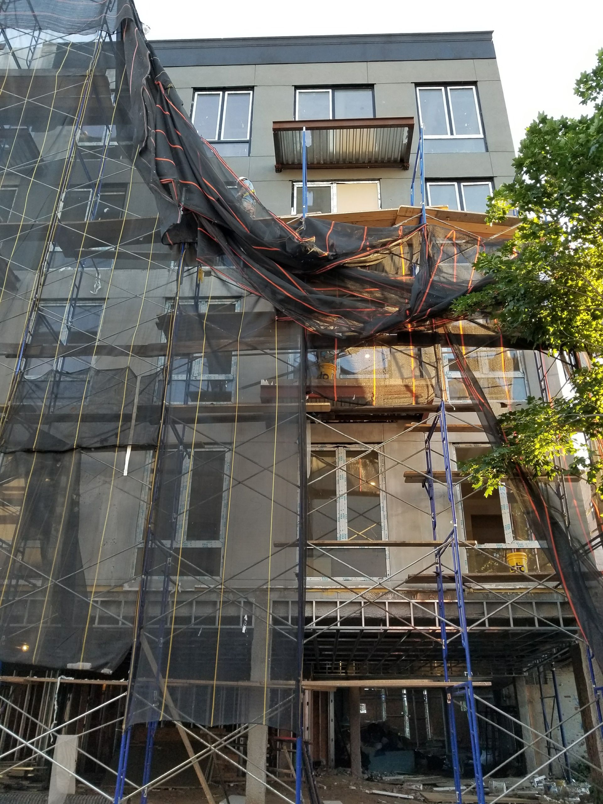 Building under construction, scaffolding and protective netting in place, gray stucco facade.